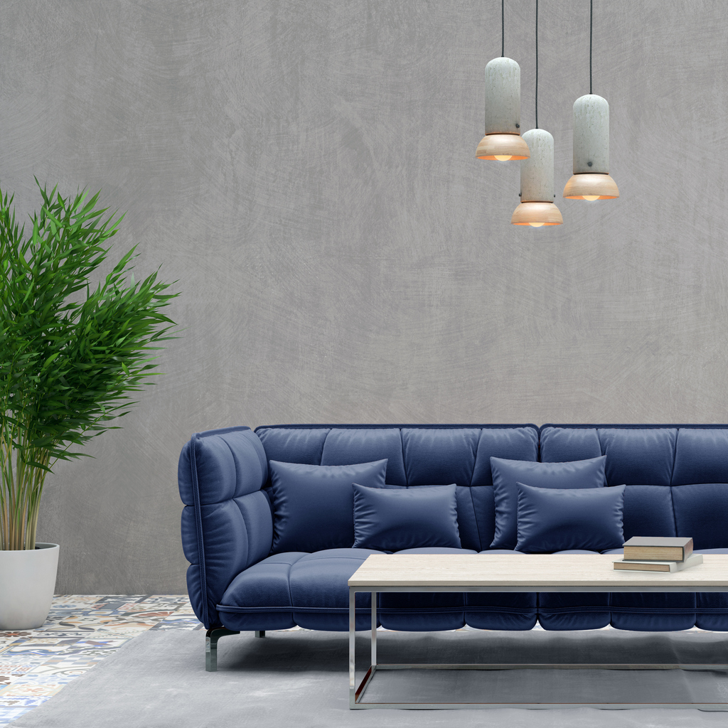 A modern living room featuring a blue sofa with matching pillows, a white coffee table with books, a large potted green plant, gray textured walls, and three hanging pendant lights.