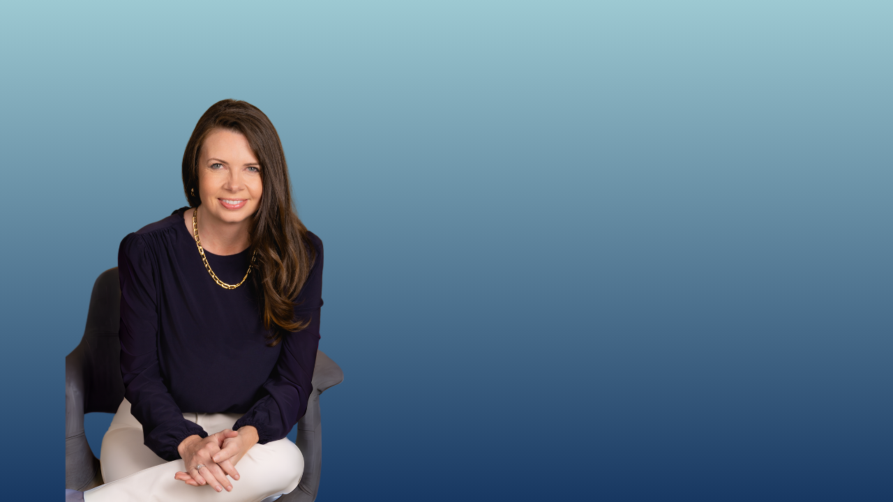 A woman with long brown hair, wearing a navy blouse and white pants, sitting on a black chair against a blue gradient background.