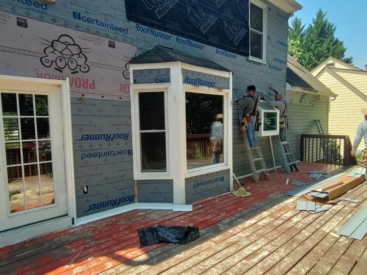 Two men work together to install new blue gray siding onto a residential home.