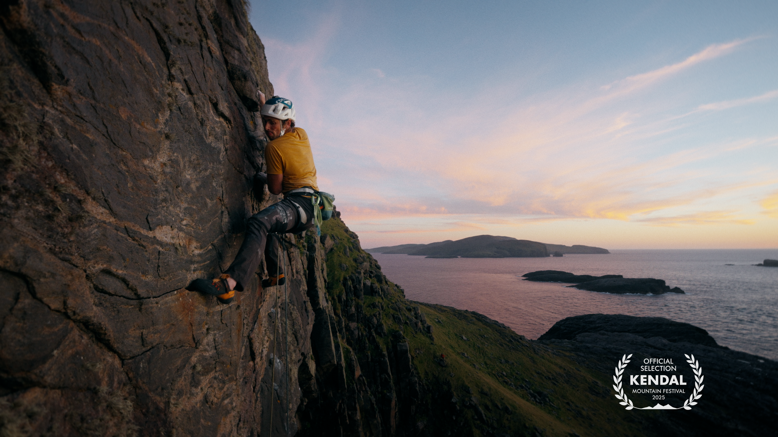 A man is climbing a steep cliff face during sunset over the ocean, wearing a helmet and climbing gear, with a small badge in the bottom right corner reading 'Official Selection Kendal Mountain Festival 2025'.