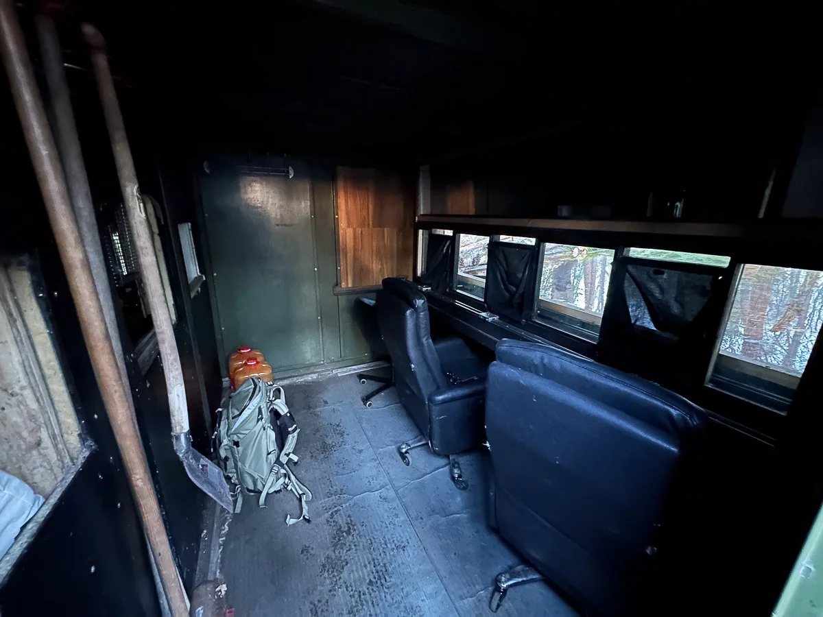 Innenansicht eines Fotoverstecks mit zwei schwarzen Bürostühlen, einer Fensterreihe, einem Rucksack und einem Kanister