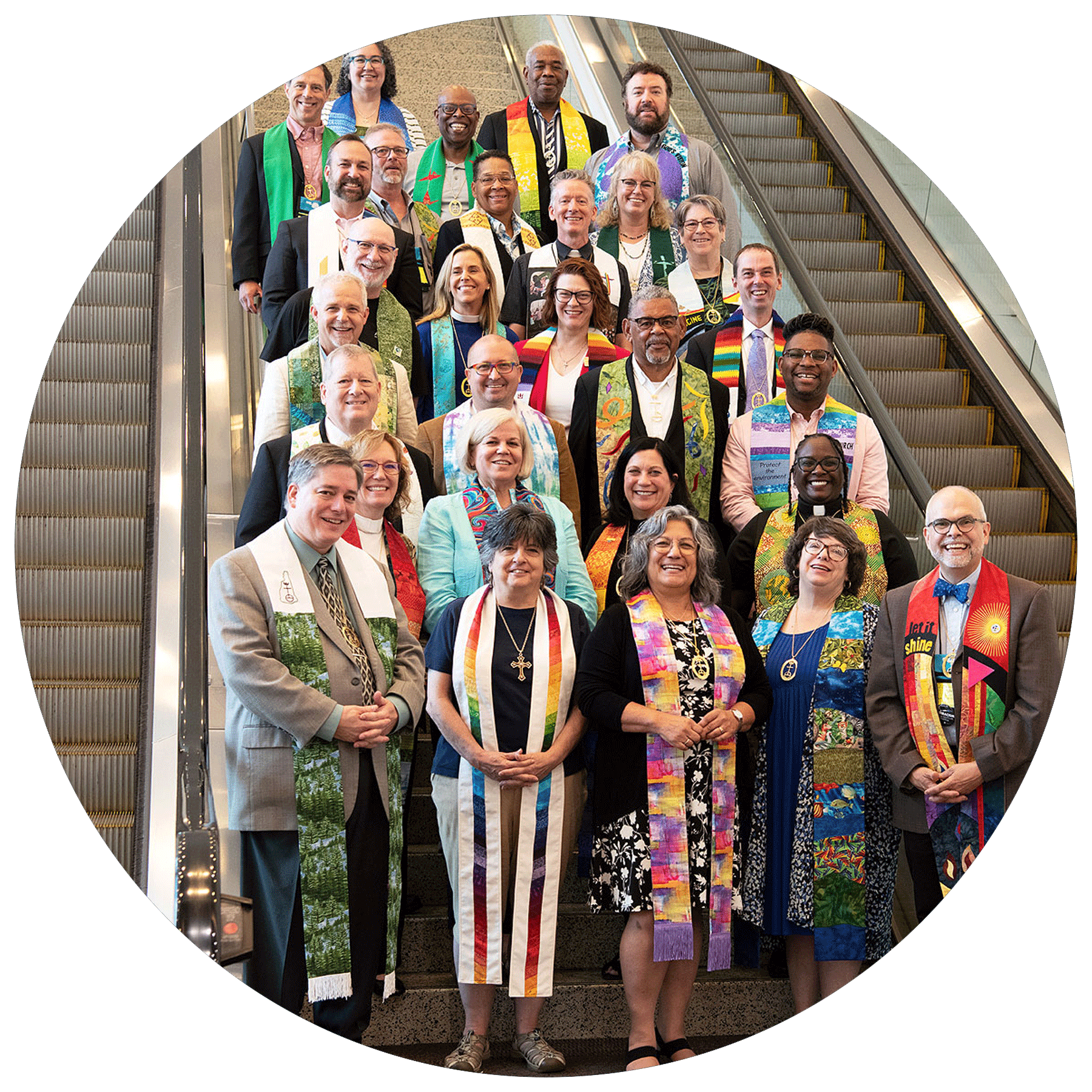 Group of diverse people posing on an indoor staircase, many wearing colorful scarves or stoles, smiling for a photo.