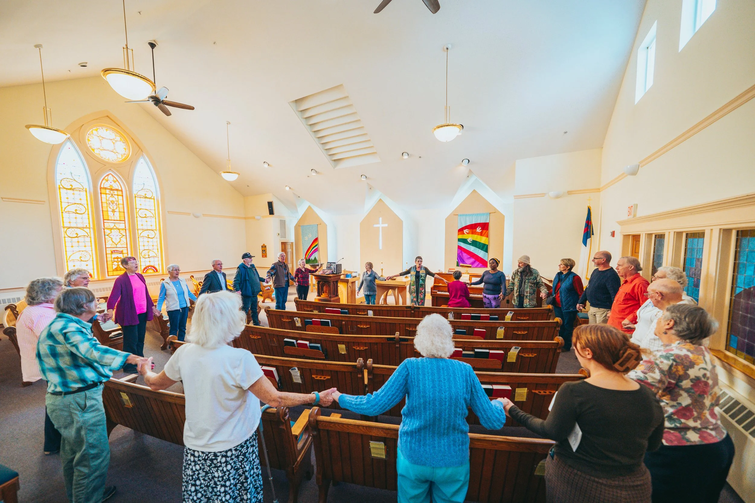 A group of diverse people holding hands in a circle inside a church with stained glass windows and wooden pews.