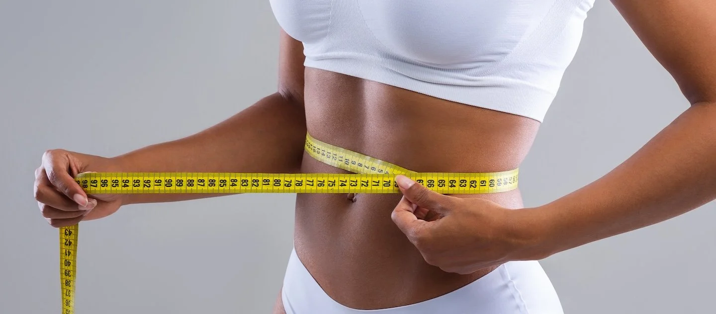 Person measuring their waist with a yellow tape measure, wearing white workout clothing.