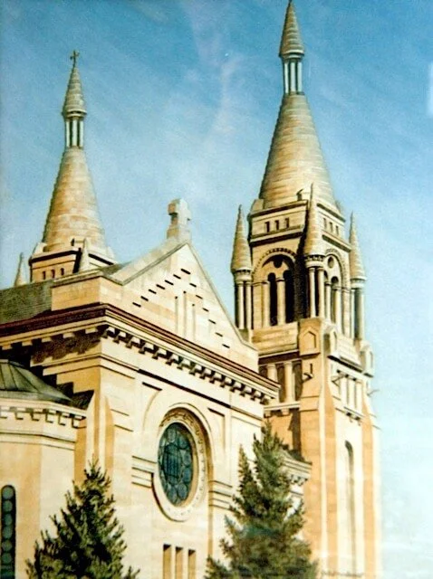 A historic church with two tall, pointed steeples under a blue sky, surrounded by trees.