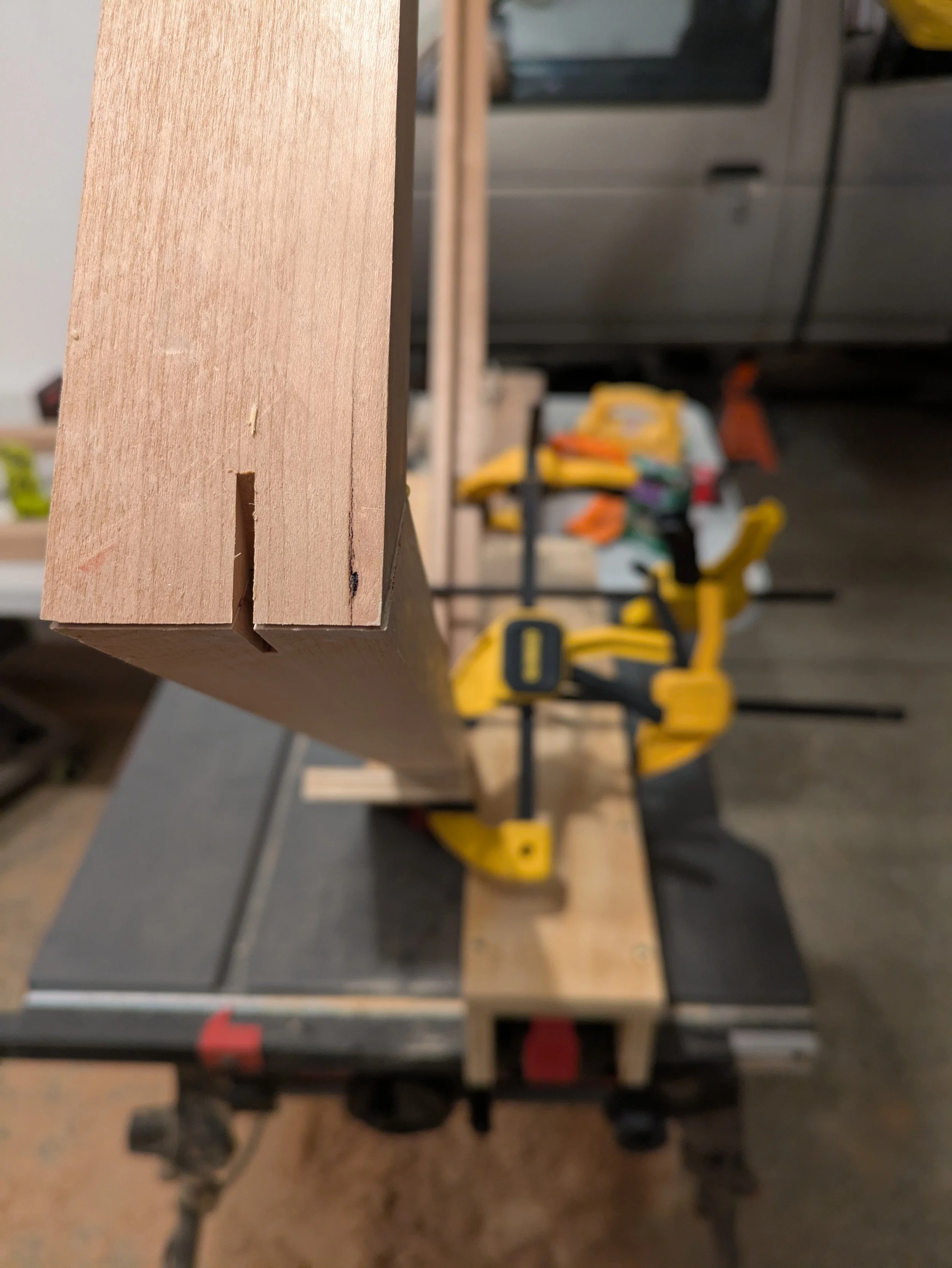 Close-up of a piece of wood clamped on a workbench with yellow clamps in a woodworking shop.
