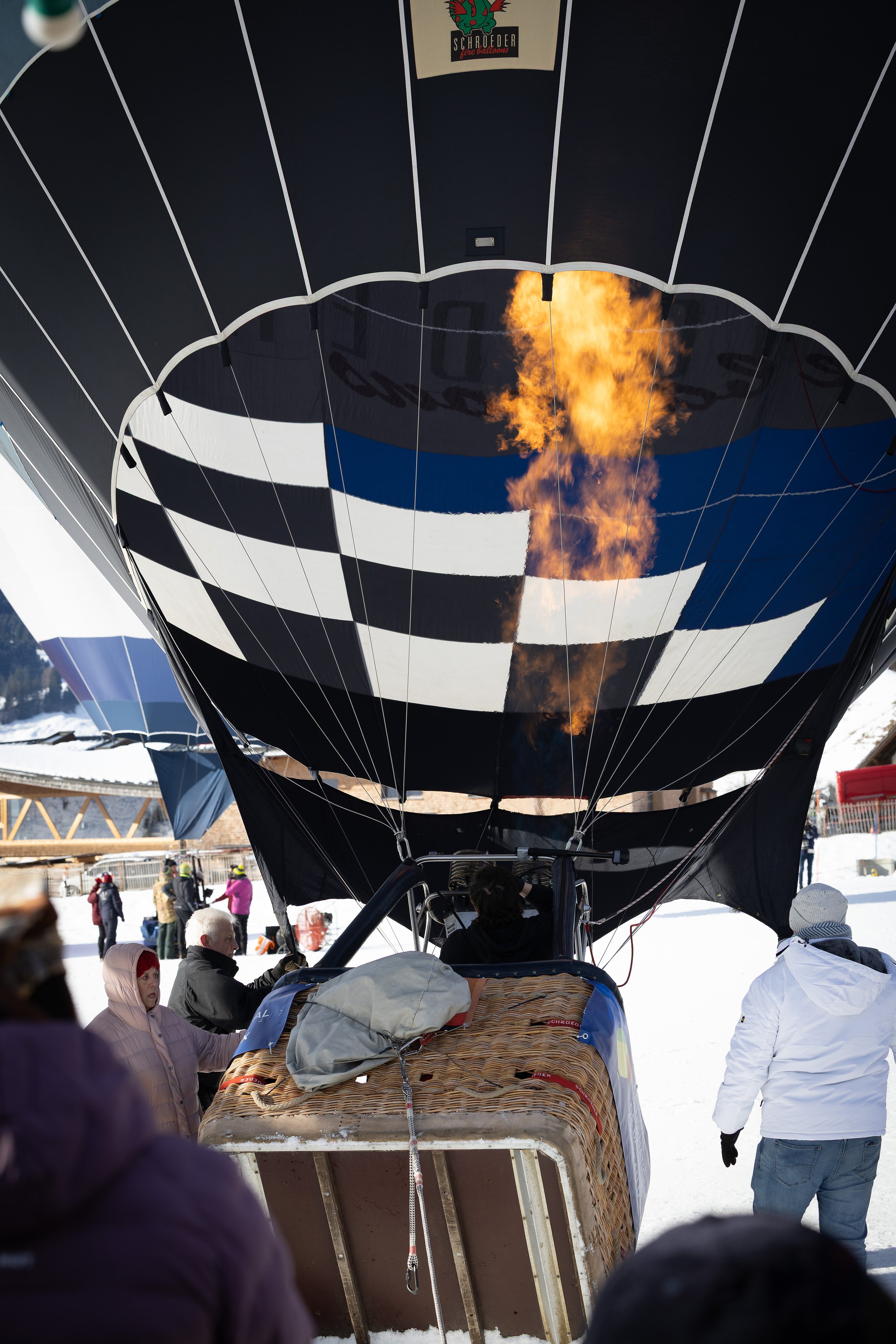 Menschen bereiten einen Heißluftballon vor, mit sichtbarer Flamme im Brenner in winterlicher Landschaft in Chateau-d'Oex.