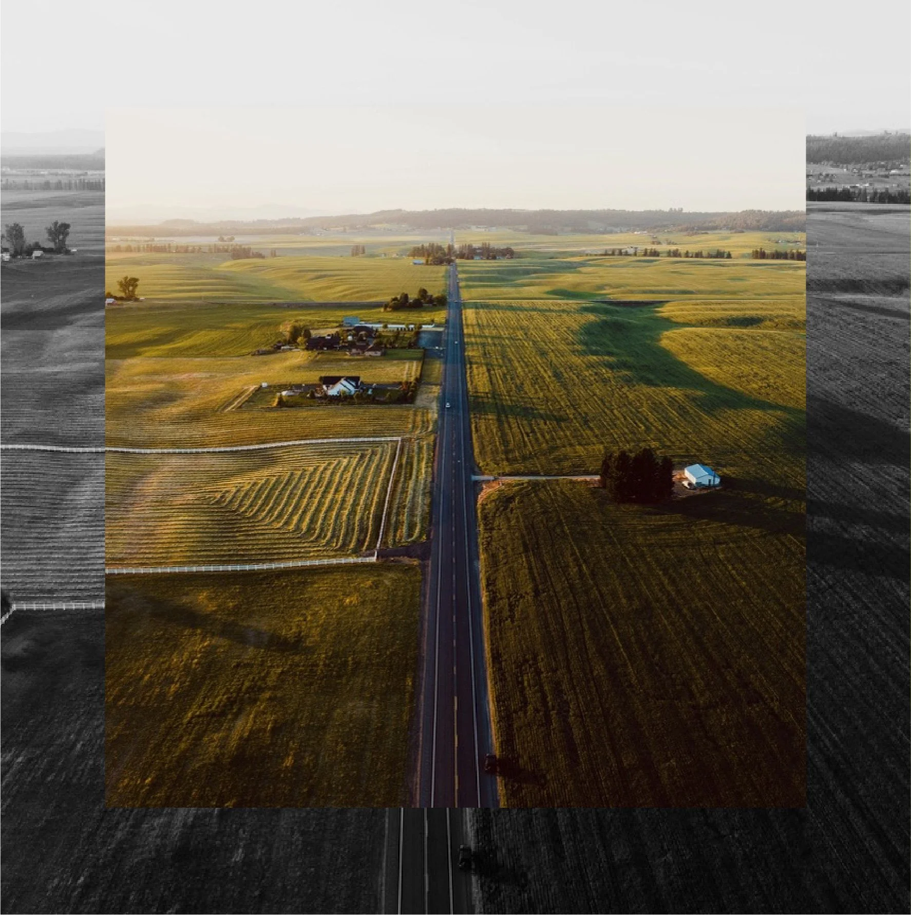 Aerial view of rural farmland with a straight highway running through the green and yellow fields, houses, and farm structures, with rolling hills in the distance during sunset.