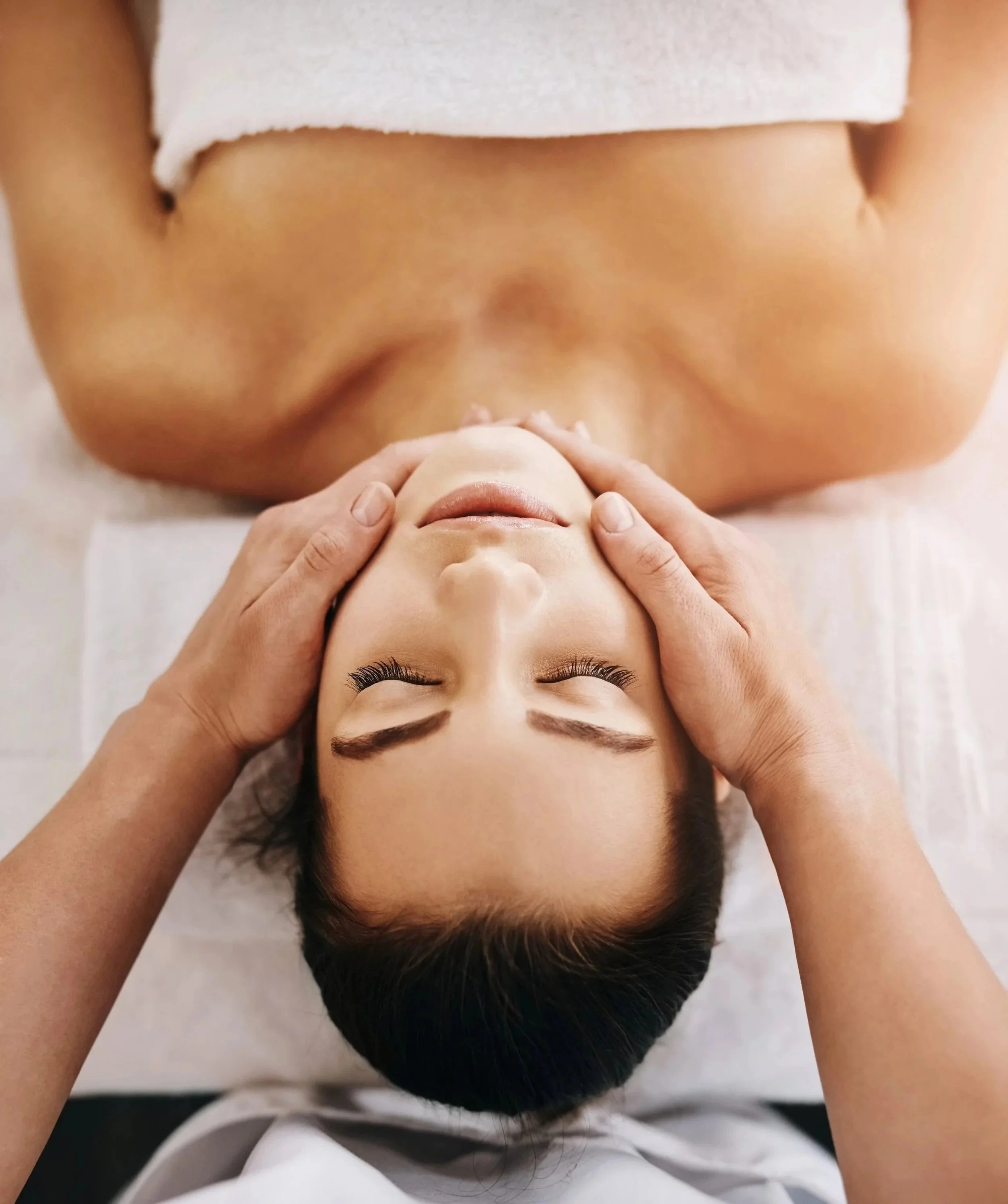 A woman receiving a massage or face treatment with a therapist applying gentle pressure to her forehead.