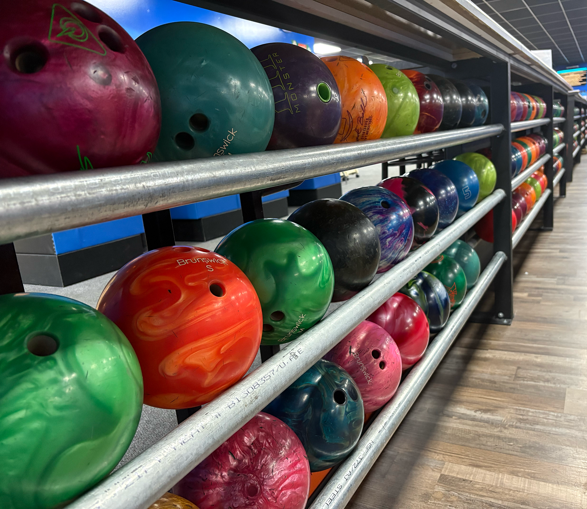 Multiple colorful bowling balls on a rack in a bowling alley.
