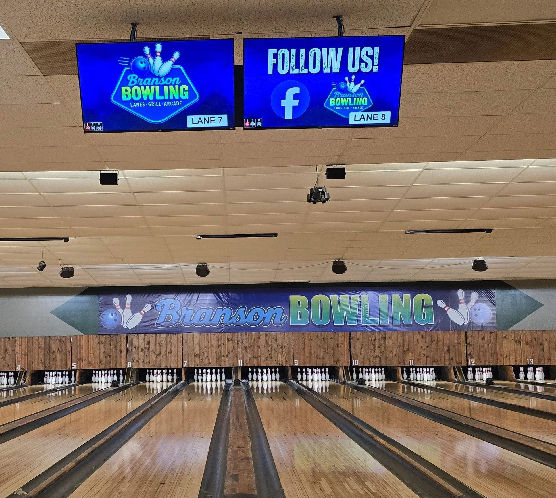 Bowling alley with lanes, pins at the end, and a banner reading 'Branson Bowling'. Two digital screens display the logo and social media info.