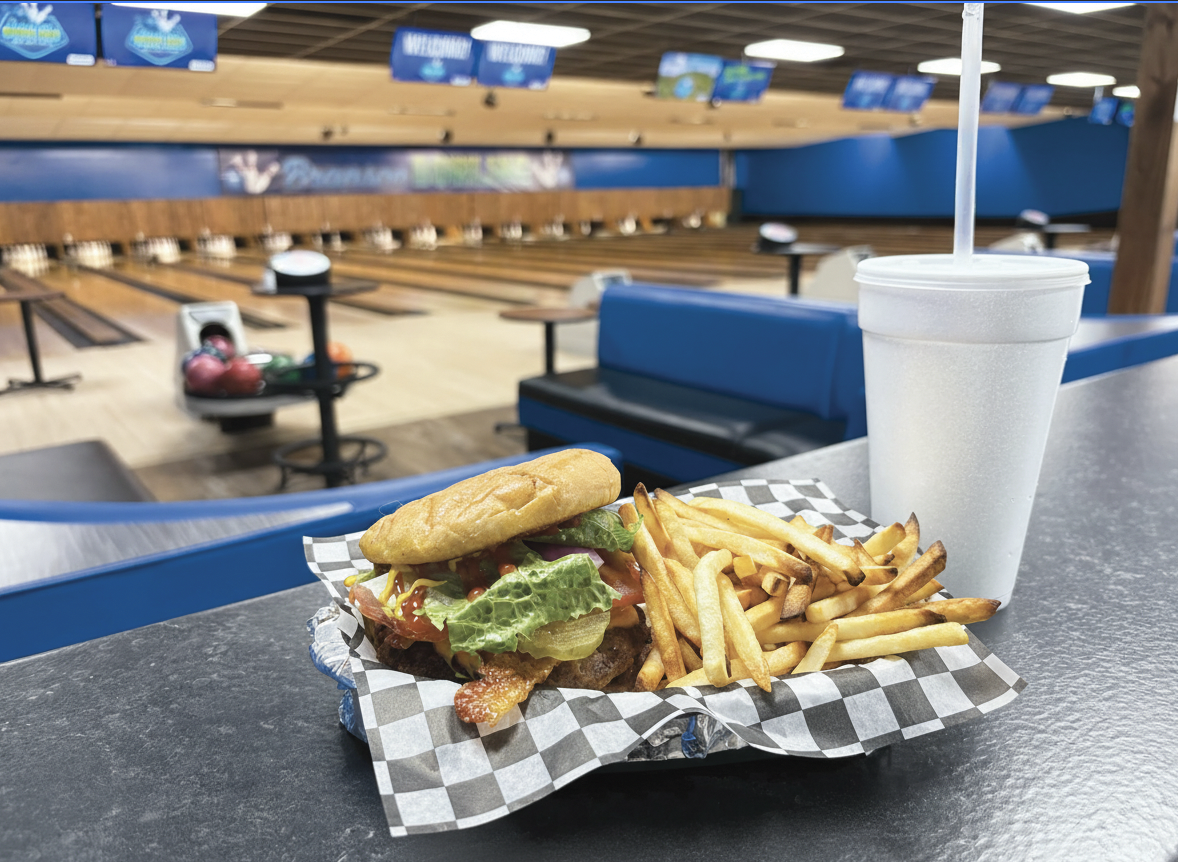 Branson Bowling, 10 Pin Bar and Grill, A burger with lettuce, tomato, bacon, and a bun, served with a side of French fries and a white foam cup with a straw, on a checkered paper-lined tray at a bowling alley.