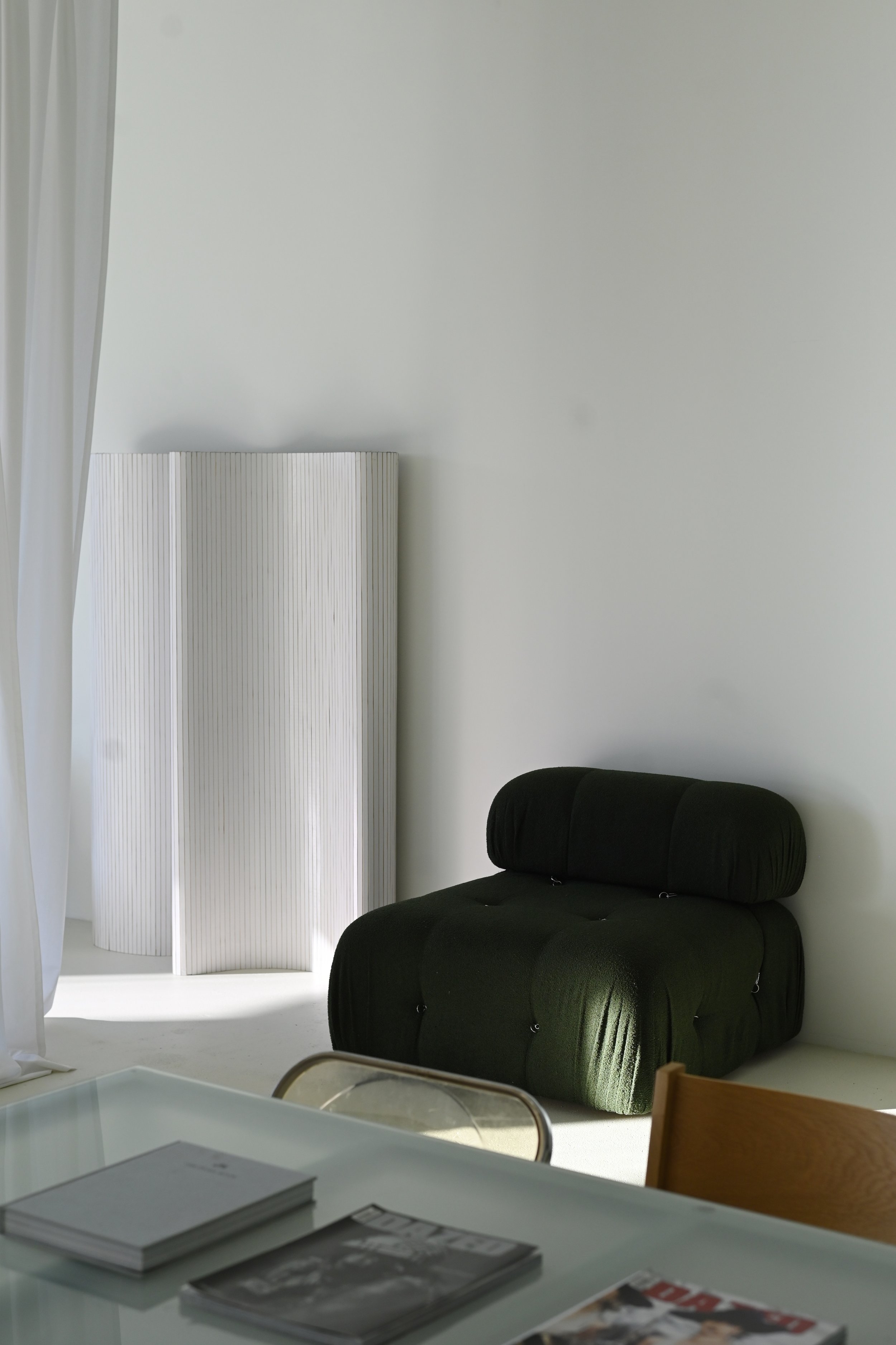 Minimalist room with black cushioned chair, white folding screen, and a table with magazines.