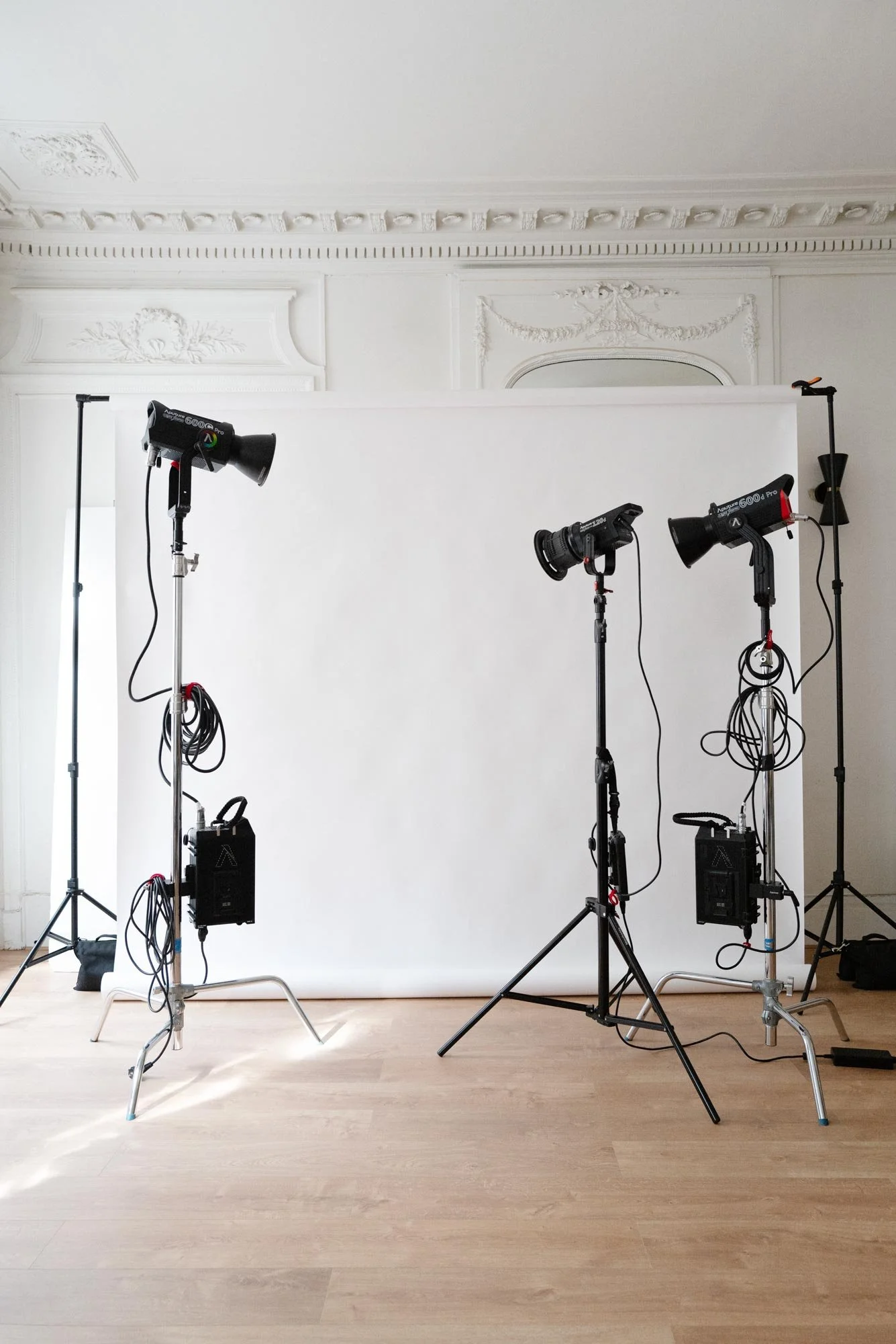Espace de photographie en intérieur avec un fond blanc, trois lampes d'éclairage sur trépieds, moulures au plafond. Studio photo L'ASSOCIÉ PARIS.