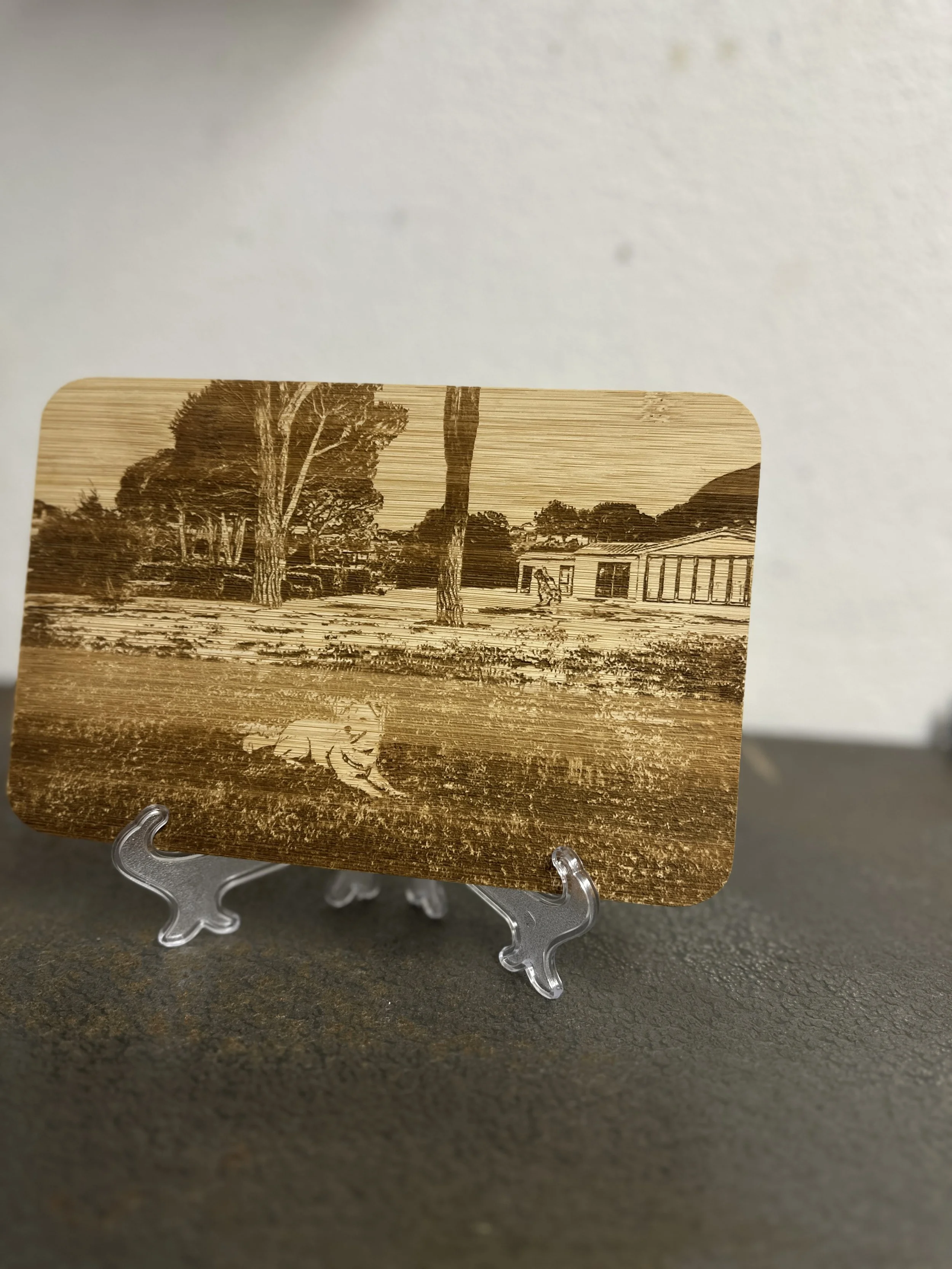 Foto di un oggetto in legno intagliato con un paesaggio di alberi, una figura di un animale e una struttura architettonica, esposto su un supporto trasparente.