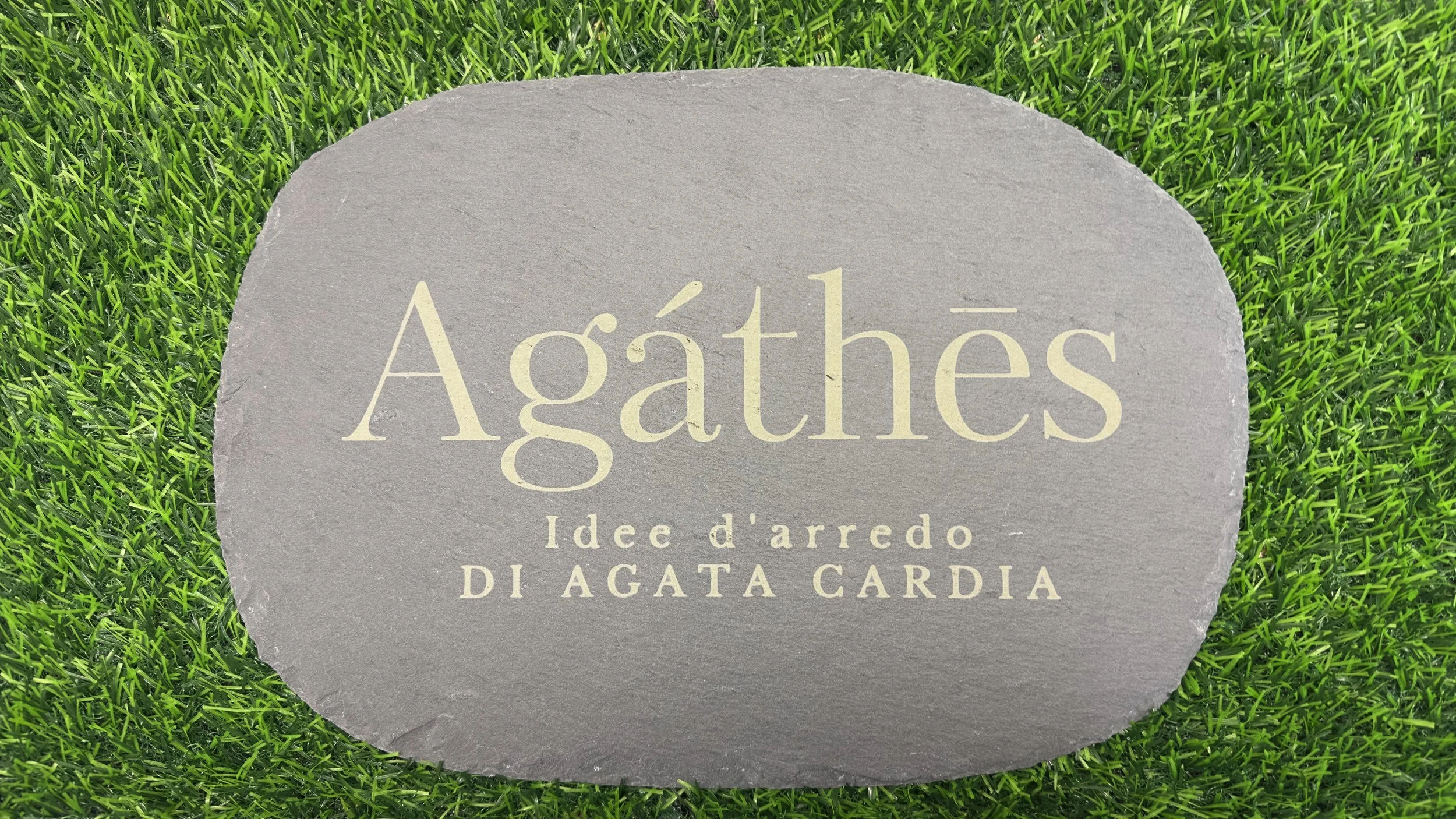 Pietra con scritta 'Agathés Idees d'arredo Di Agata Cardia' circondata da erba verde