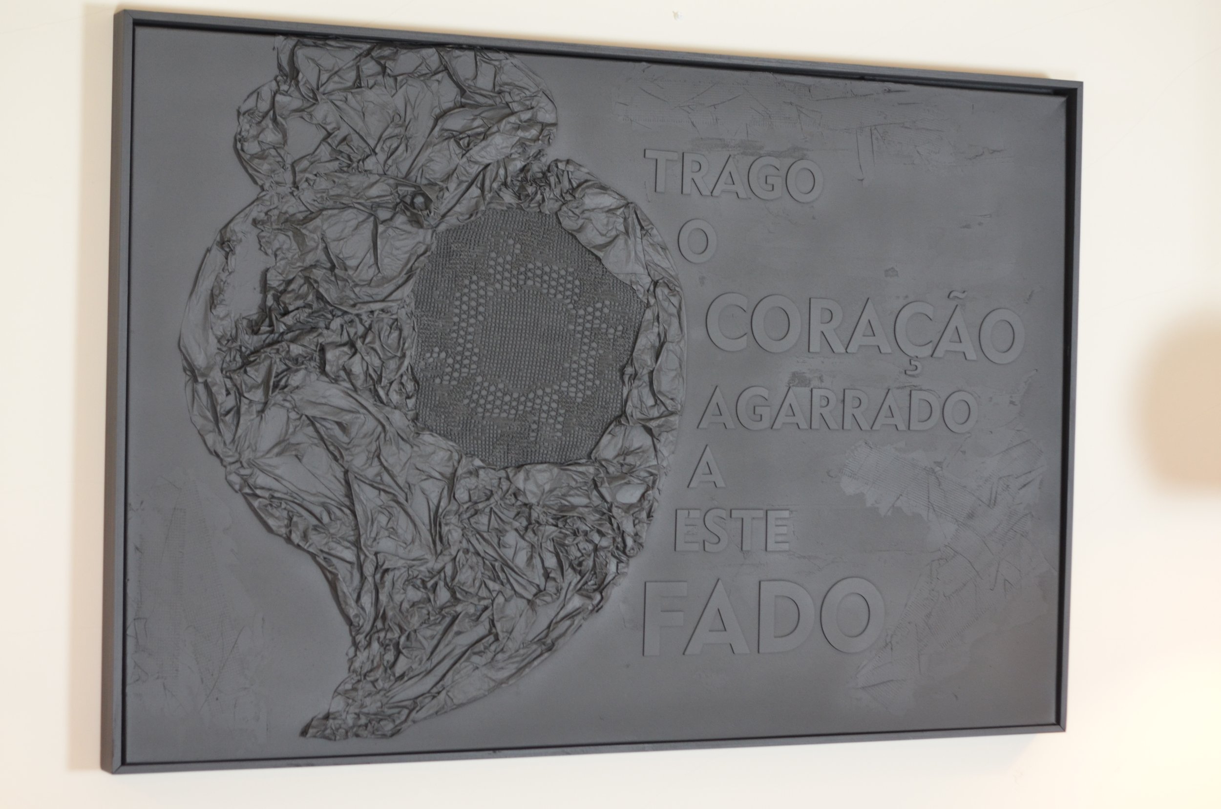 Quadro da série FADO, em preto com um coração feito com relevo de papel amassado e rendas e uma inscrição do autor LU.S "Trago o coração a agarrado a este fado".