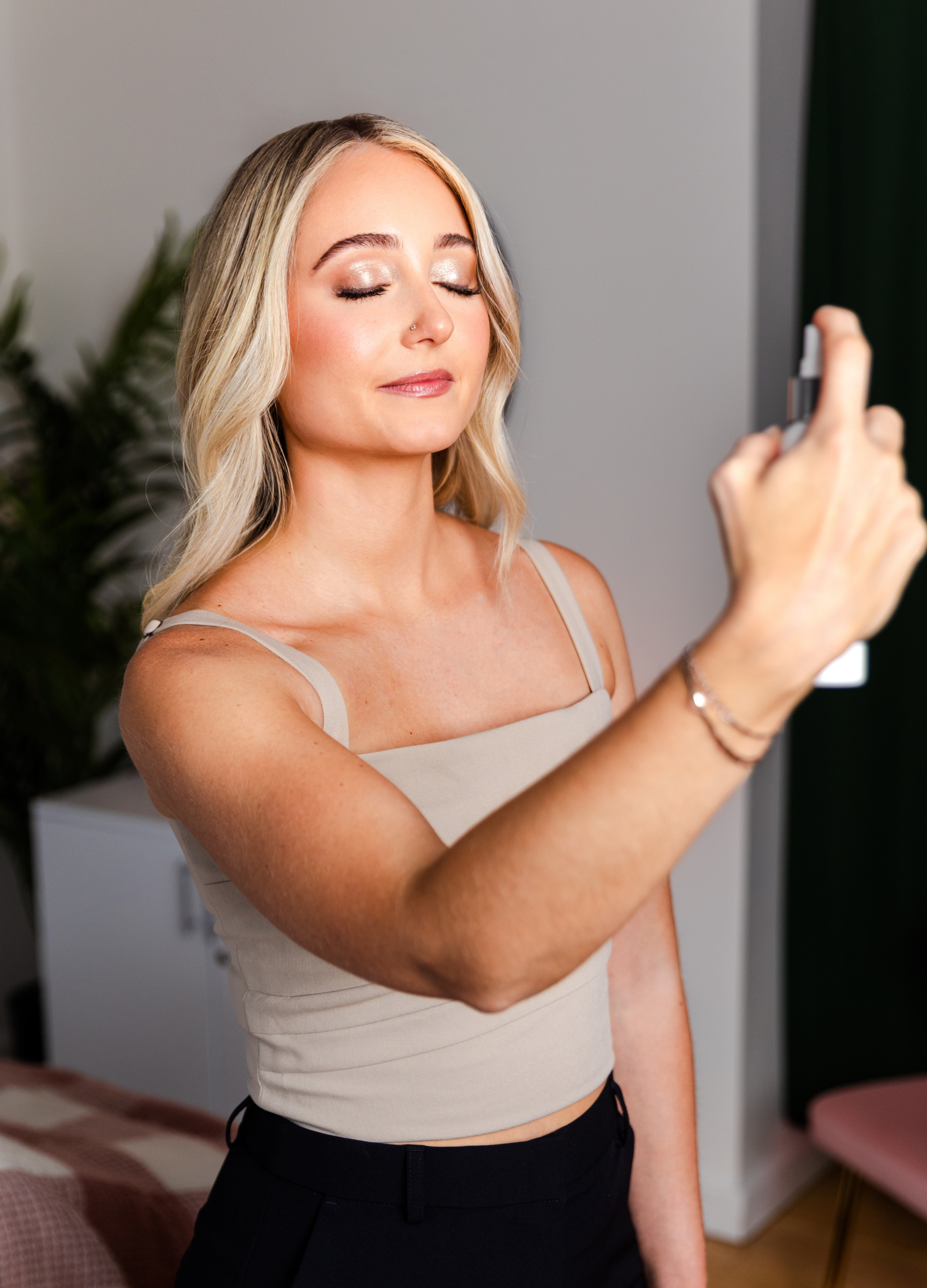A young woman with blonde hair and closed eyes taking a selfie with her phone in a room.