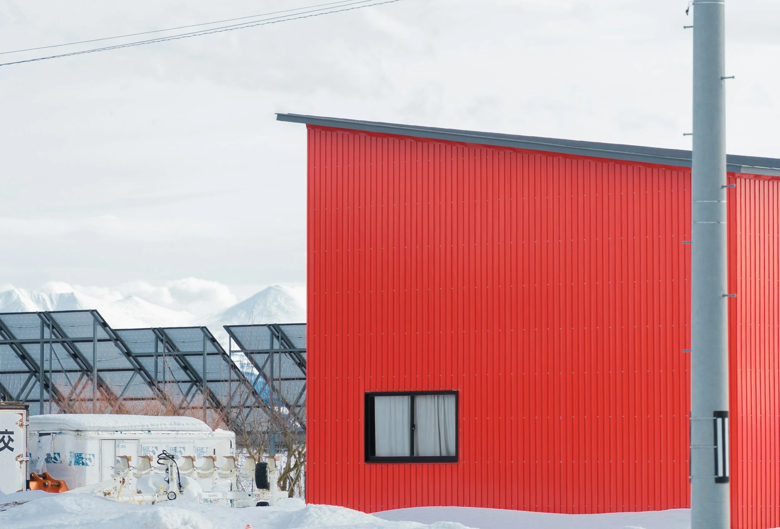 Dwelling showing red siding and low sloped roof with solar panels in the background