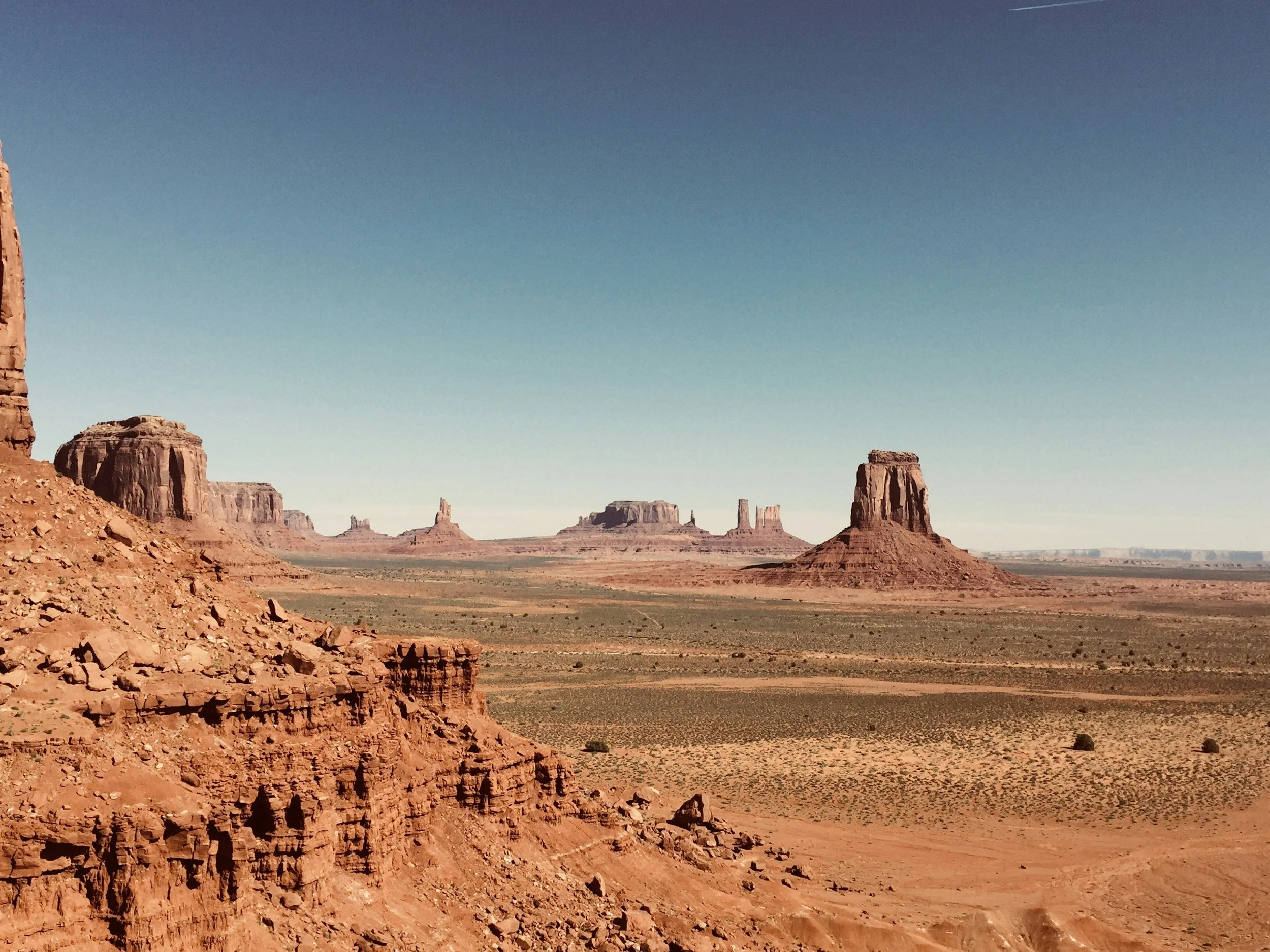 Desert landscape with large red rock formations and buttes under a clear blue sky.