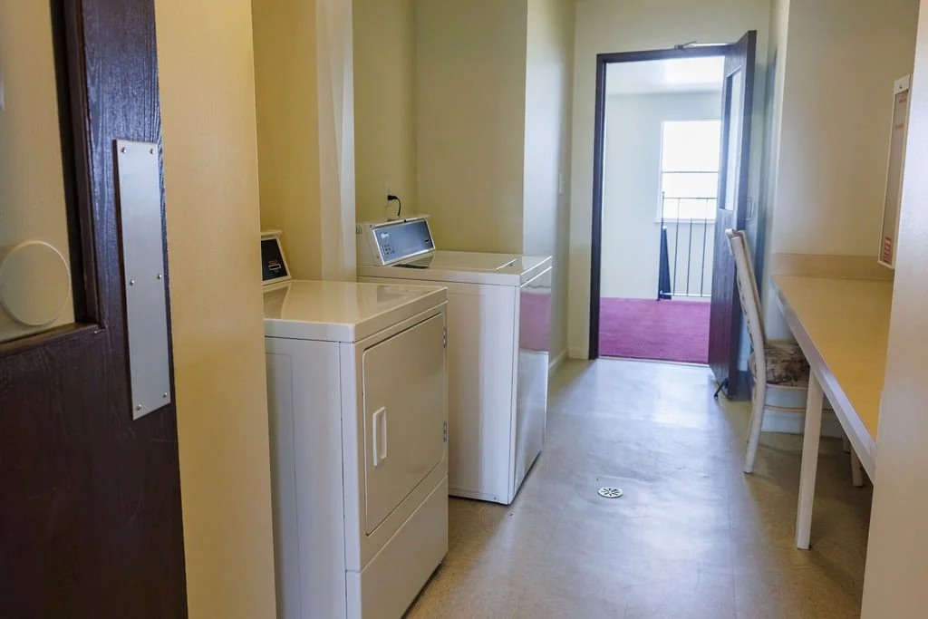 Small laundry room with a washer and dryer, a desk with a chair, and a door leading to a balcony with a railing.