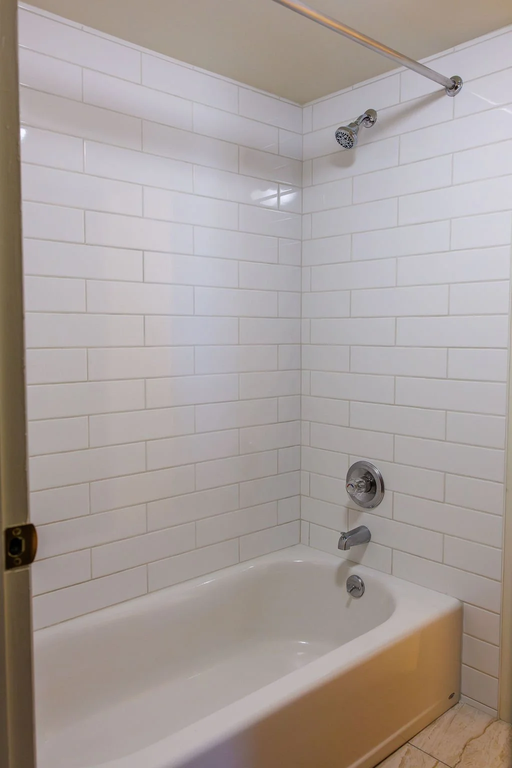 Bathroom with white subway tile walls, a bathtub with a curved edge, and a chrome showerhead and faucet.