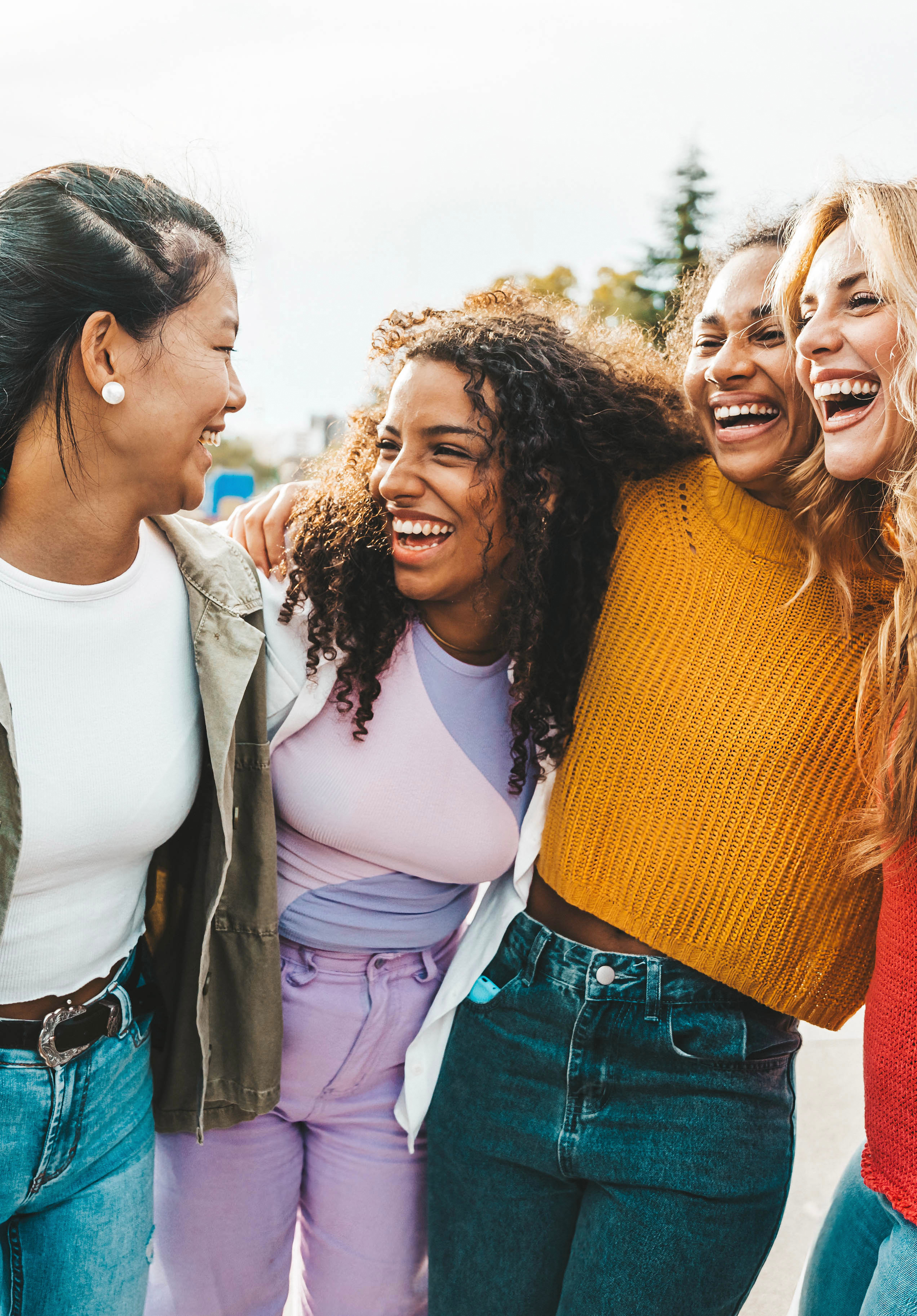 Four women smiling and laughing together outdoors, close-up shot.