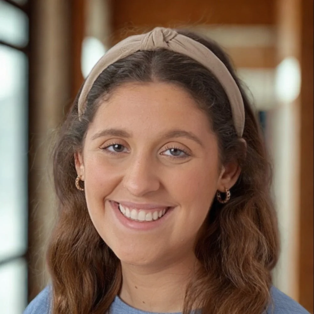 A man with glasses, a nose ring, and dark hair with some gray, looking off to the side in a room with a white wall and a plant in the background.