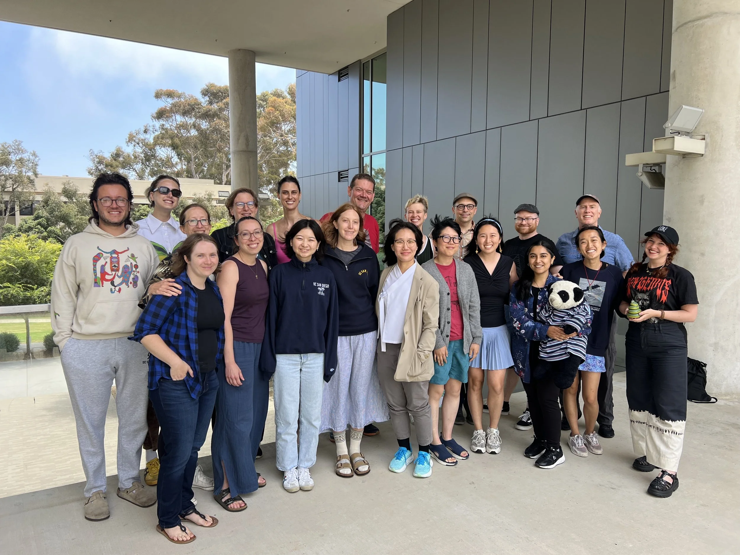 Group of diverse people standing outdoors in front of a modern building, smiling for a photo.