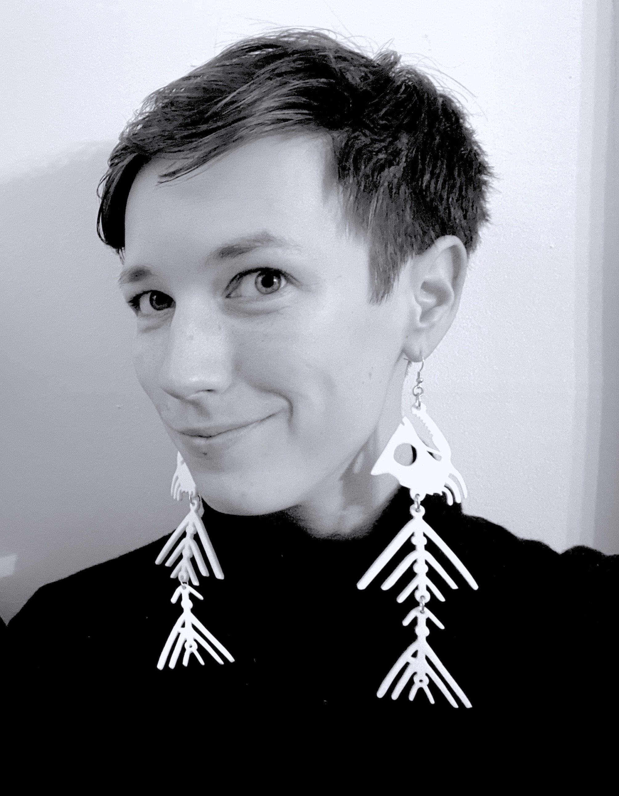 A black and white photograph of Lara Elena Donnelly, a writer with short hair wearing large, intricate earrings.
