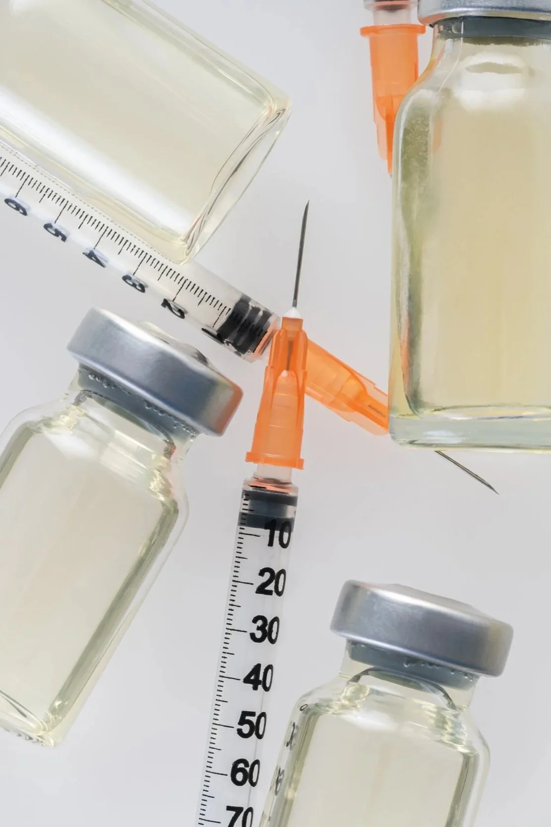 Medical vials and syringes on a white surface, with some filled with a clear liquid.