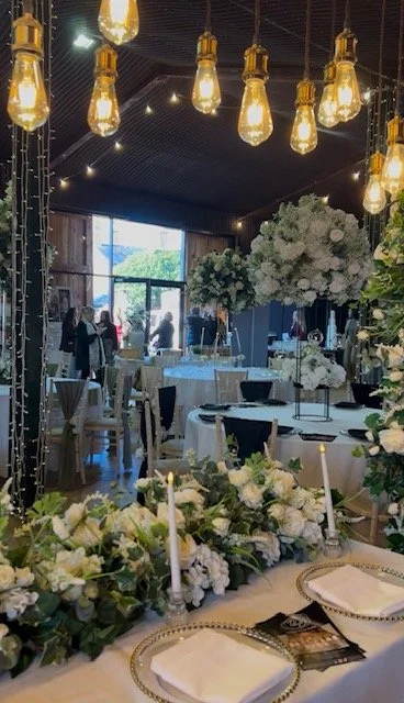 open day image inside stock farm barn showing couples and visitors moving around the beautifully displayed barn with an abundance of white flowers and candles on each table