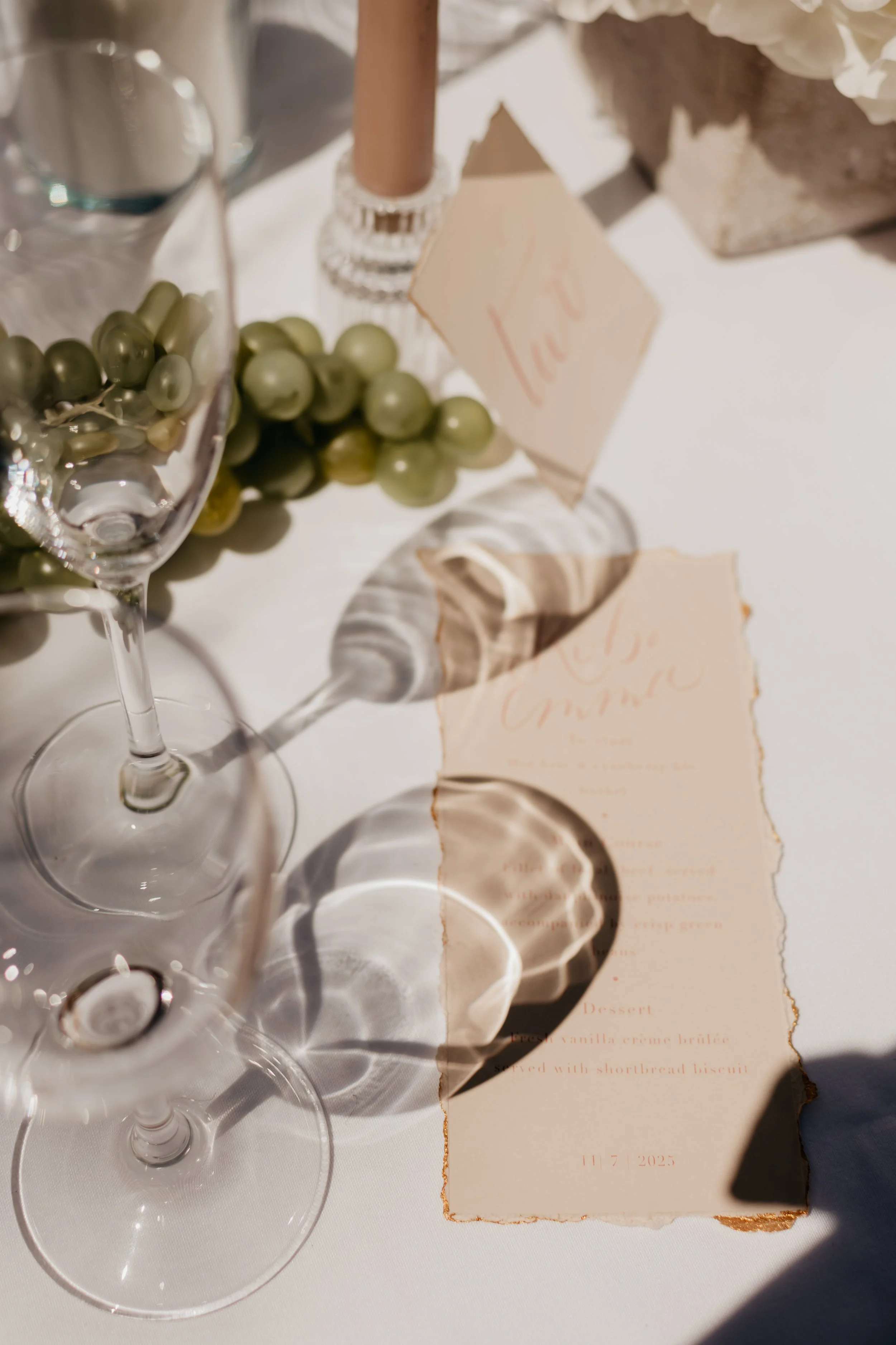 a blury image with the sunshine bluring the details through a wine glass. a menu with pink text is visible though the glass