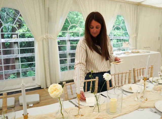 elizabeth placing place cards on a decorated wedding breakfast table decorated with white flowers in a marquee