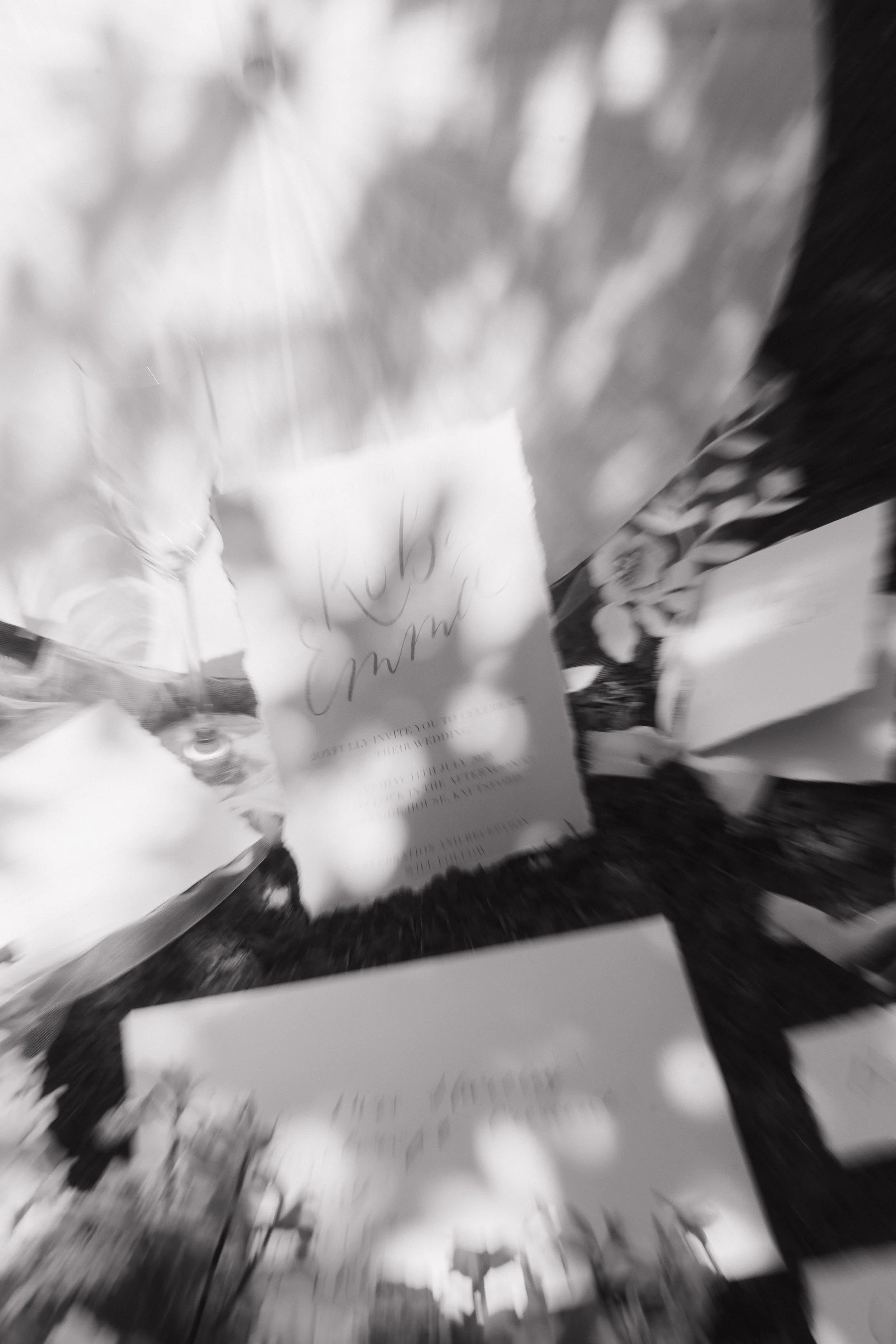 Blurred image showing a handwritten note on a piece of paper, placed on a wooden surface with outdoor light and shadows.