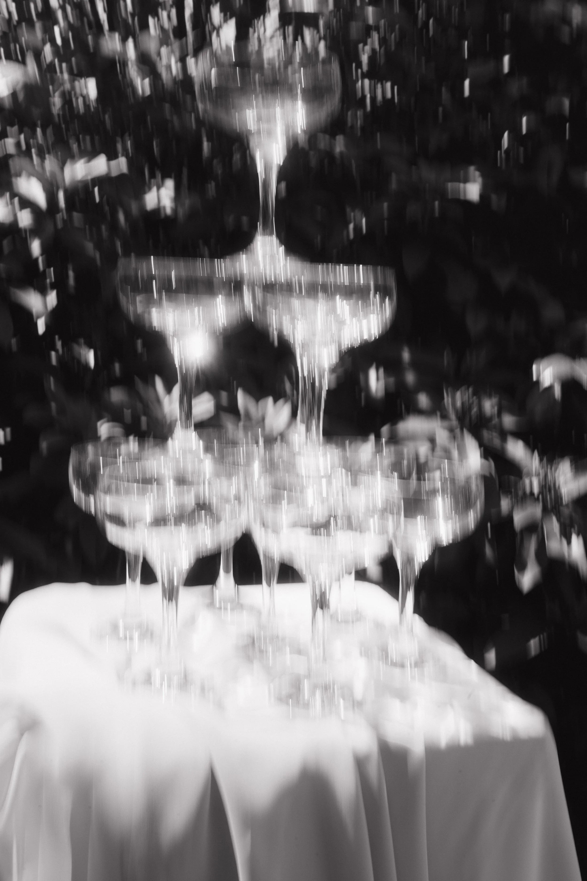A tiered champagne glass pyramid on a table, with a white tablecloth, surrounded by a confetti-filled background.