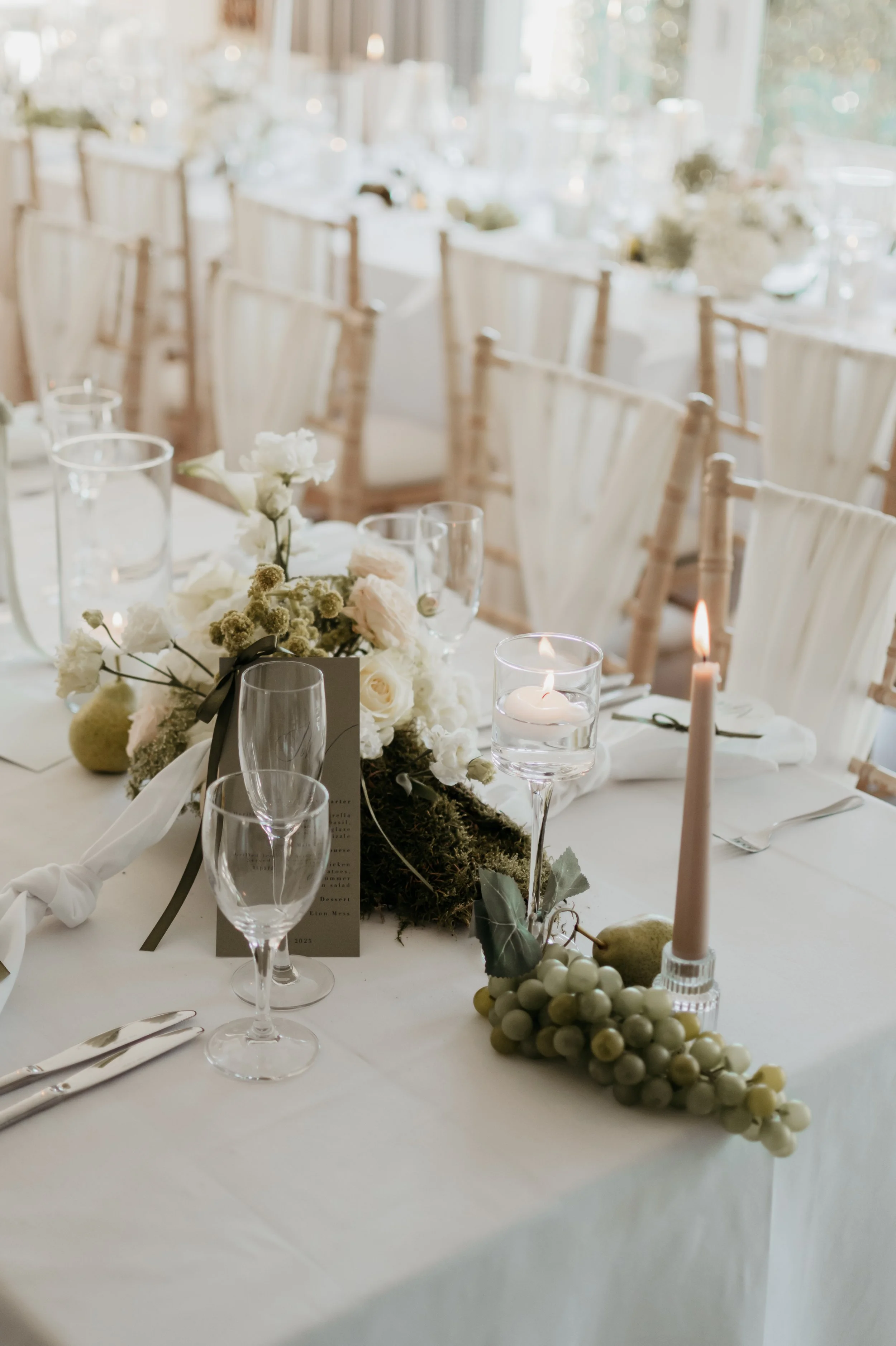 Elegant banquet table set with white flowers, candles, and glassware in a light-filled room
