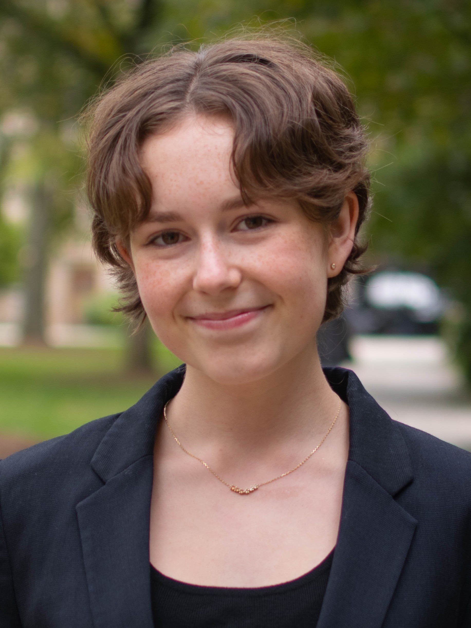 A white, feminine student with brown hair stands outside, smiling at the camera.