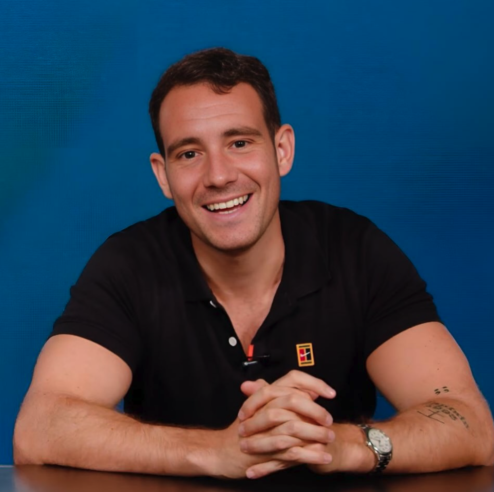 A man with a beard and short hair smiling and resting his head on his hand during a video call.
