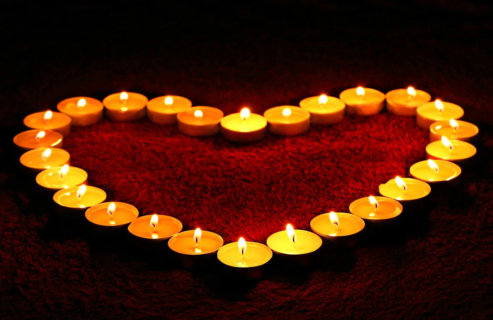 Heart-shaped arrangement of glowing tea light candles on a dark surface.