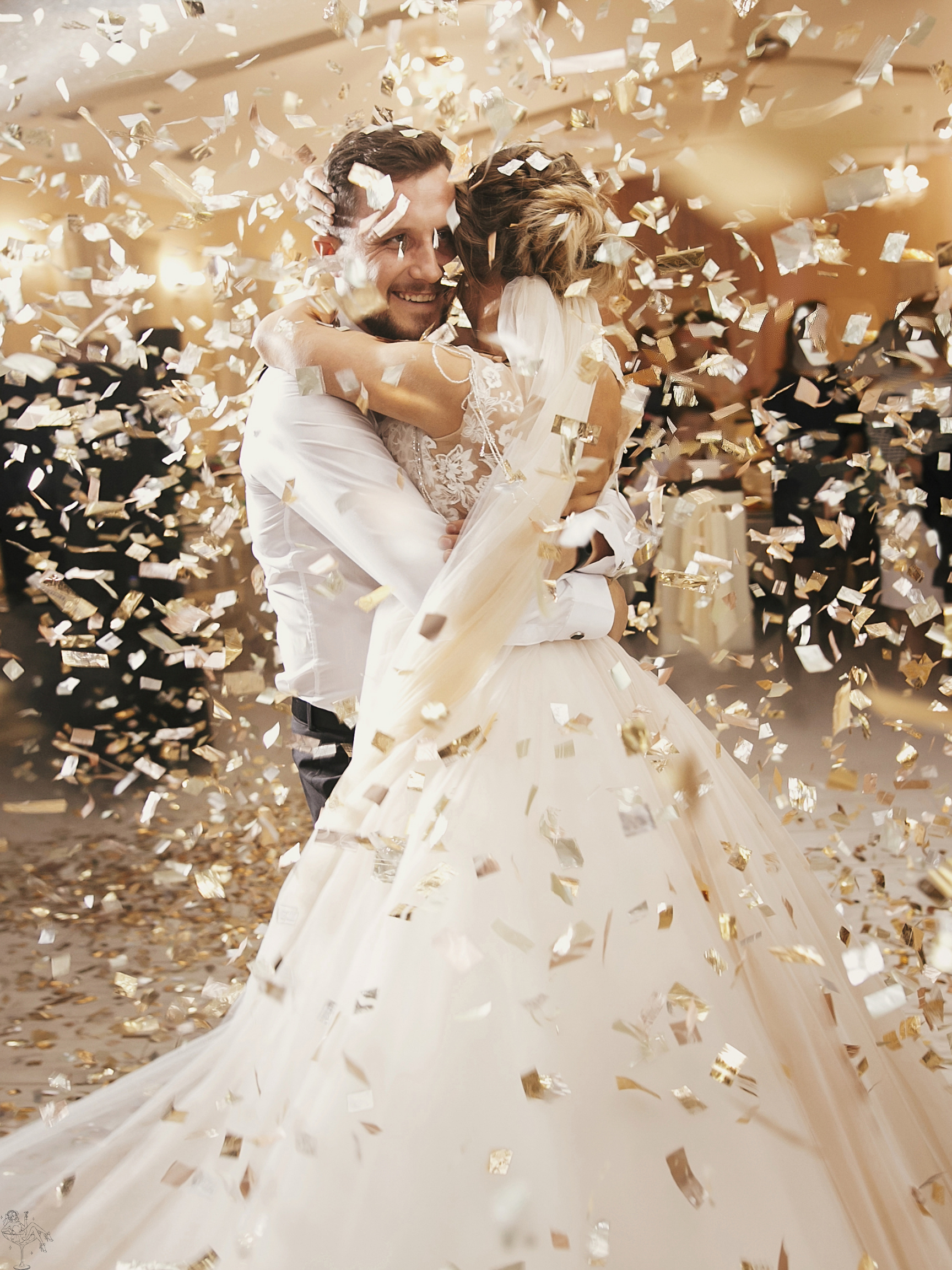 A newlywed couple sharing a joyful embrace during their wedding celebration surrounded by falling gold confetti.