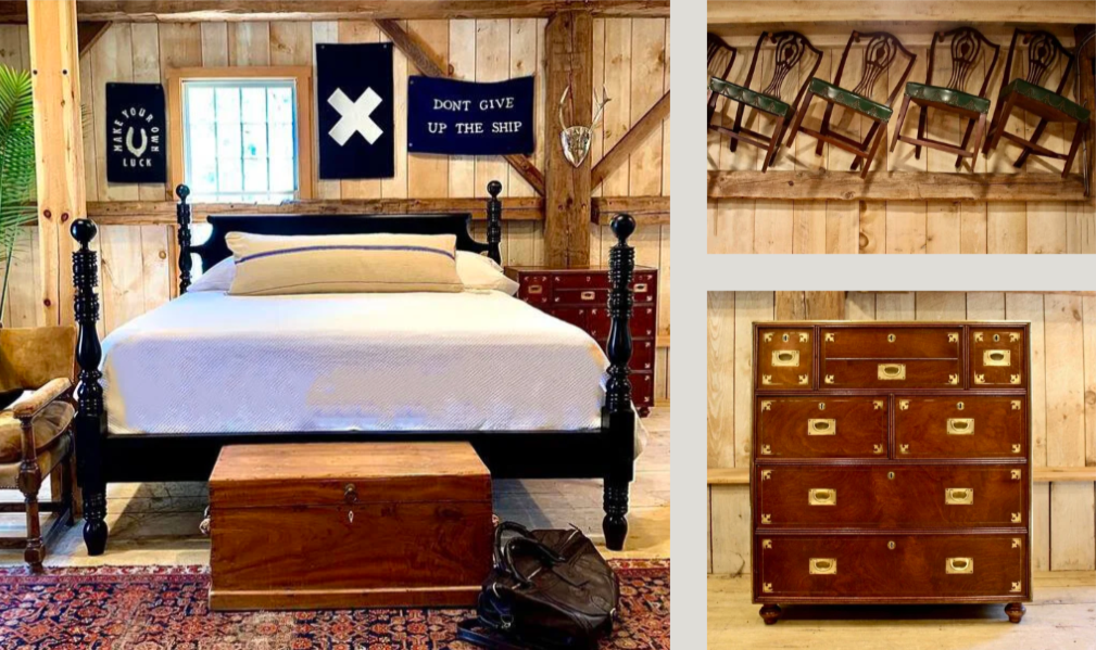 A rustic bedroom with a black four-poster bed, a wooden chest at the foot, and a floral rug. The wall has nautical-themed artwork and a window. To the right, there are four wooden chairs mounted on the wall and a vintage wooden dresser with brass accents.