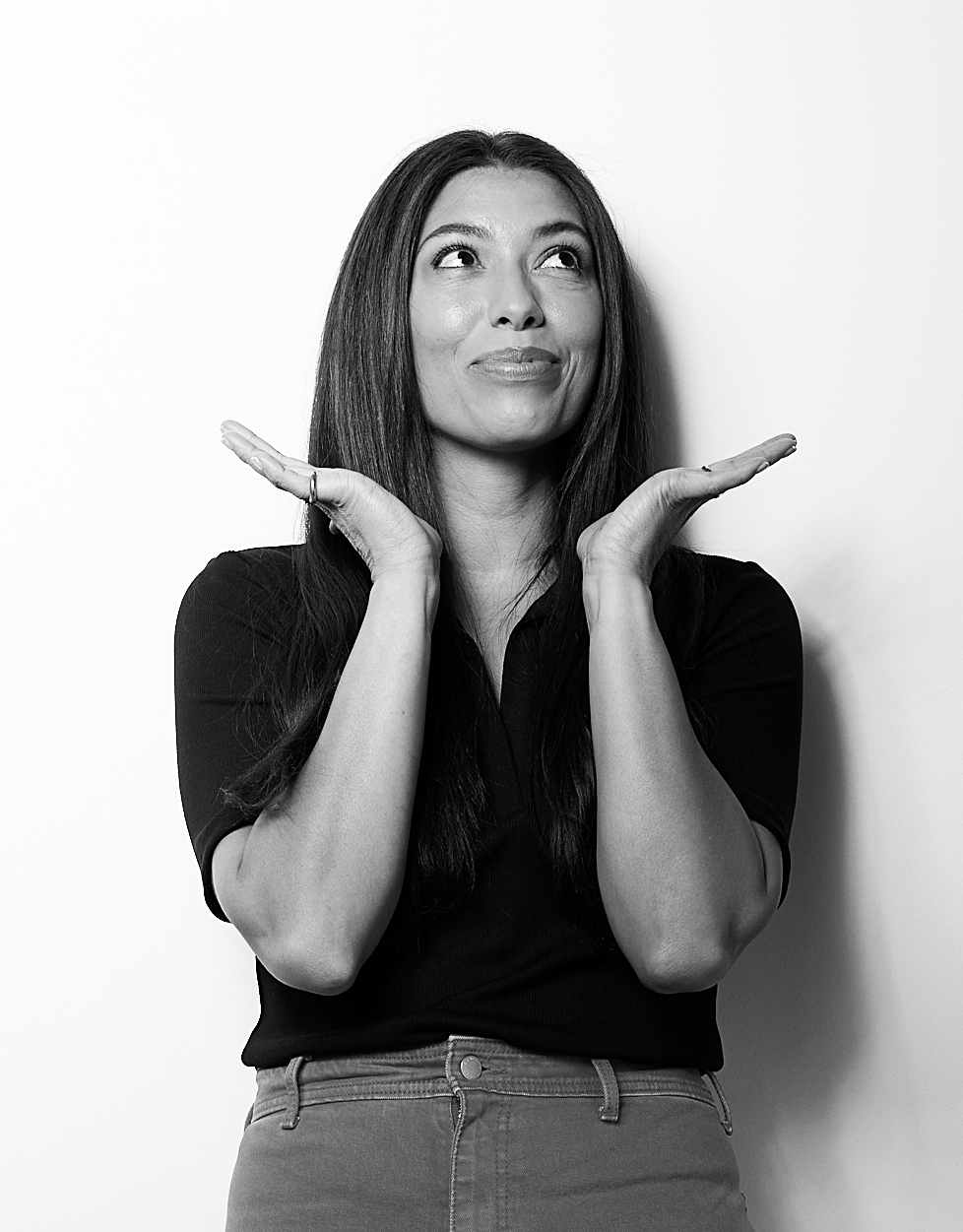 Photo of Jasmine Proaño | A woman with long dark hair making a playful expression, with her hands under her chin and looking upward.