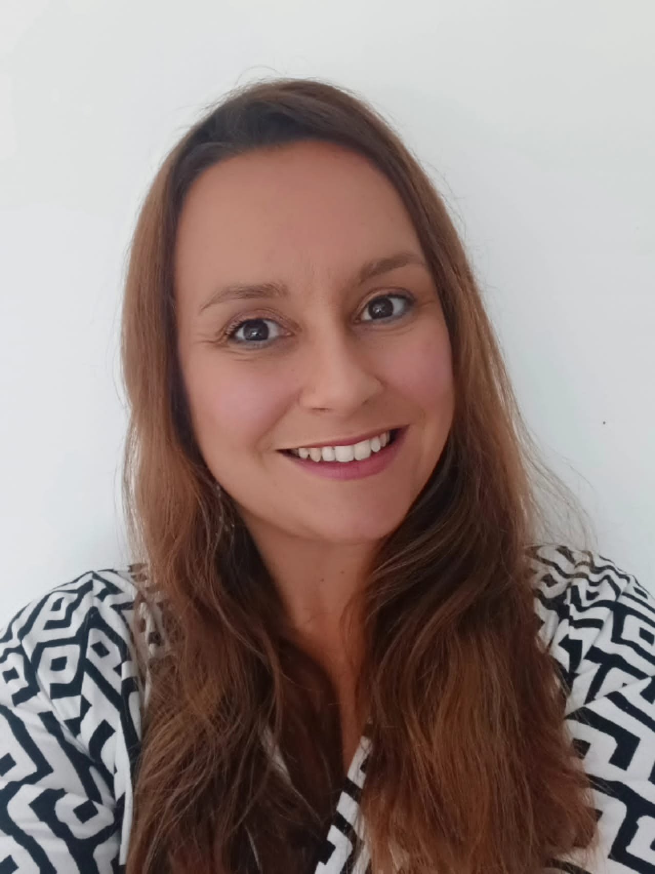 A woman with long brown hair smiling in front of a white background.