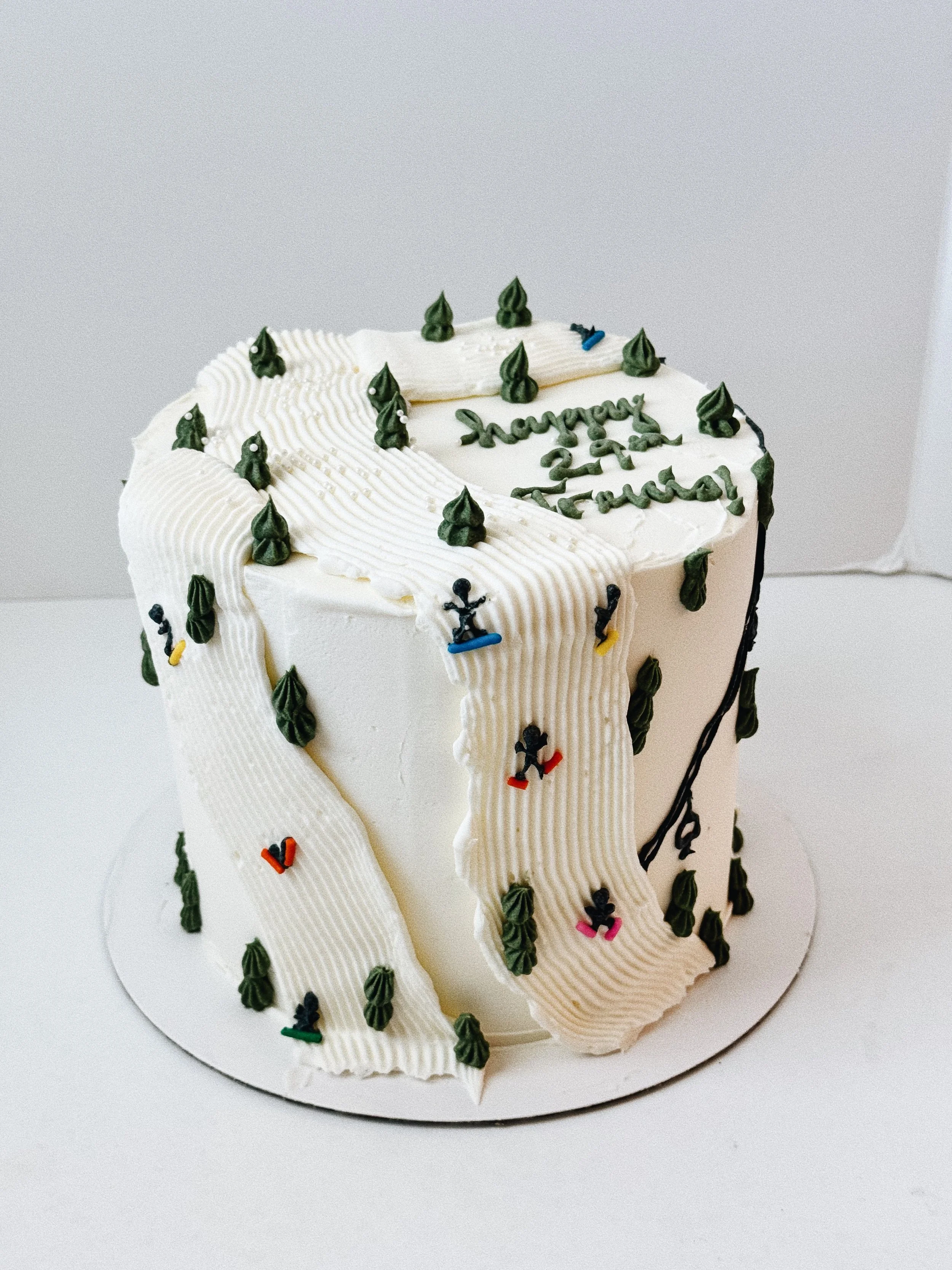 White birthday cake with green piping, small skate-themed decorations, and a message that reads 'Happy 27th, Jade'.