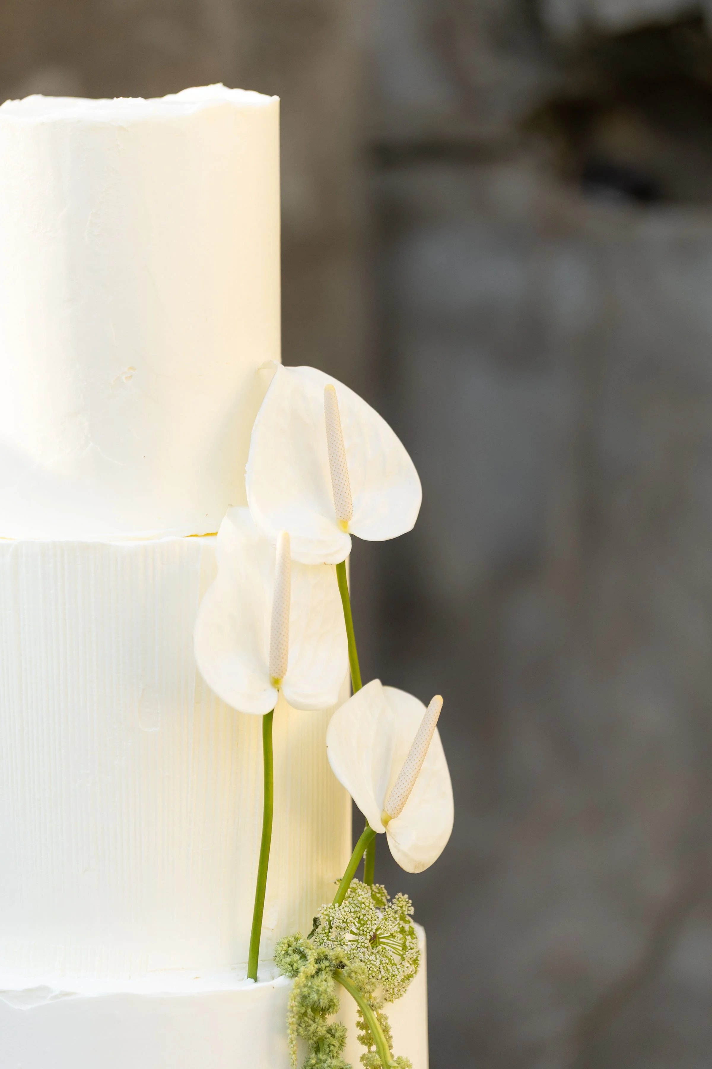 A white wedding cake decorated with white anthurium flowers and green foliage.
