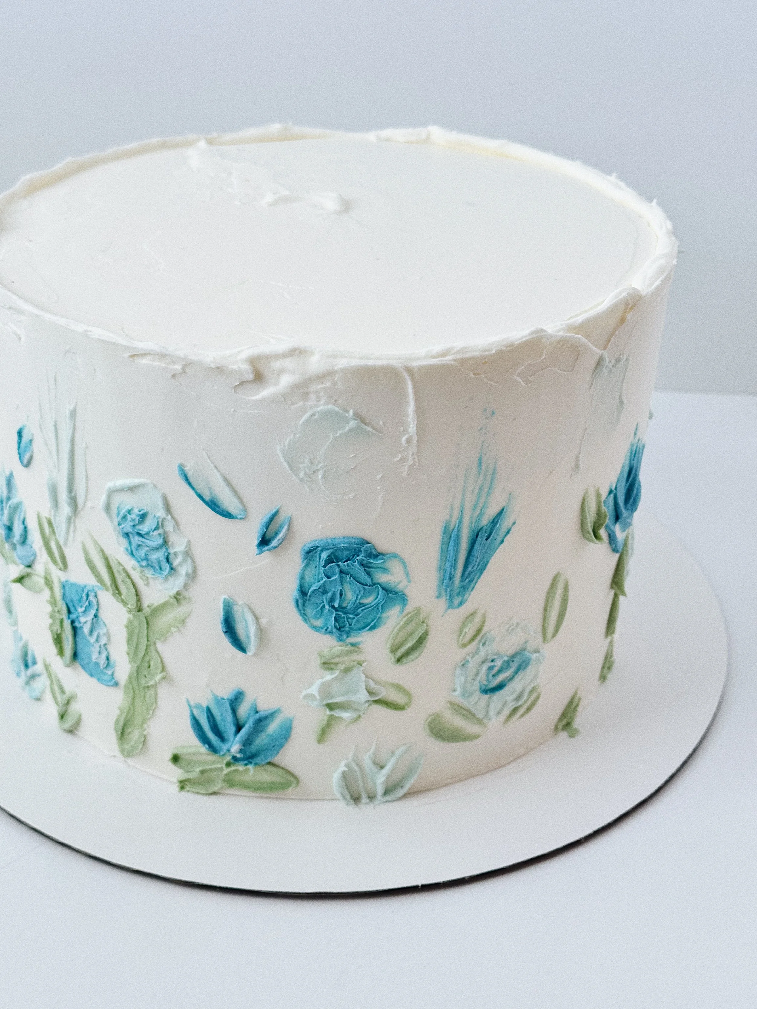 A round white frosted cake decorated with blue and green flower designs.