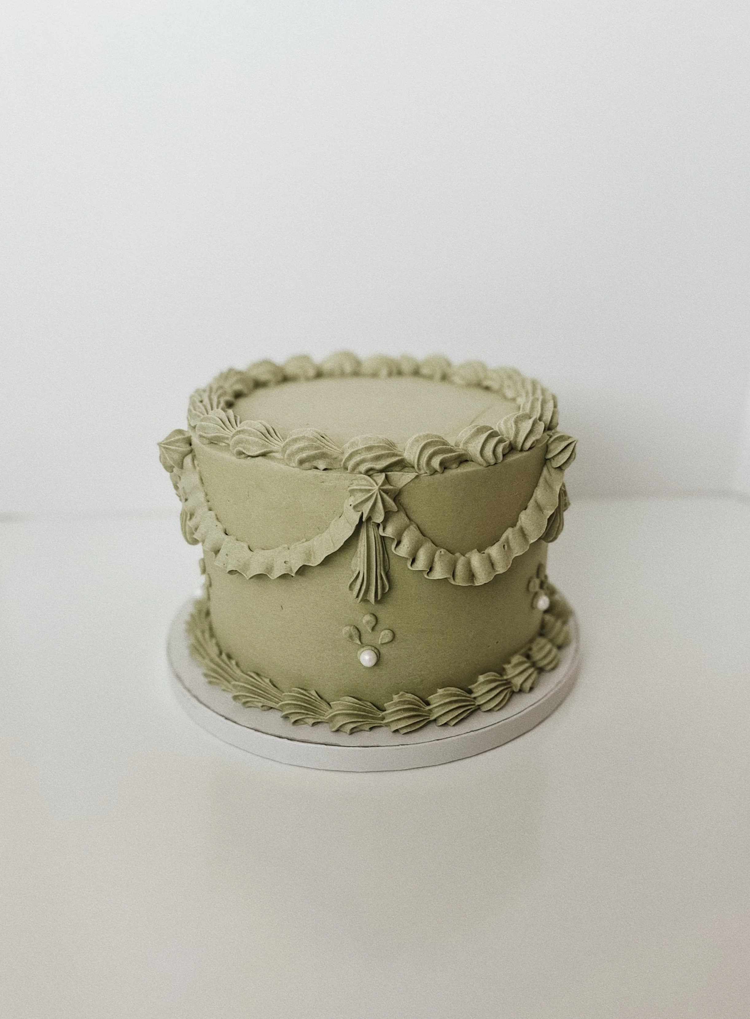 A decorated green cake with piped frosting, pearls, and ornate icing accents, set on a round white base.
