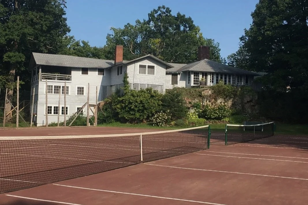 Tennis courts with a house in the background surrounded by trees and greenery.