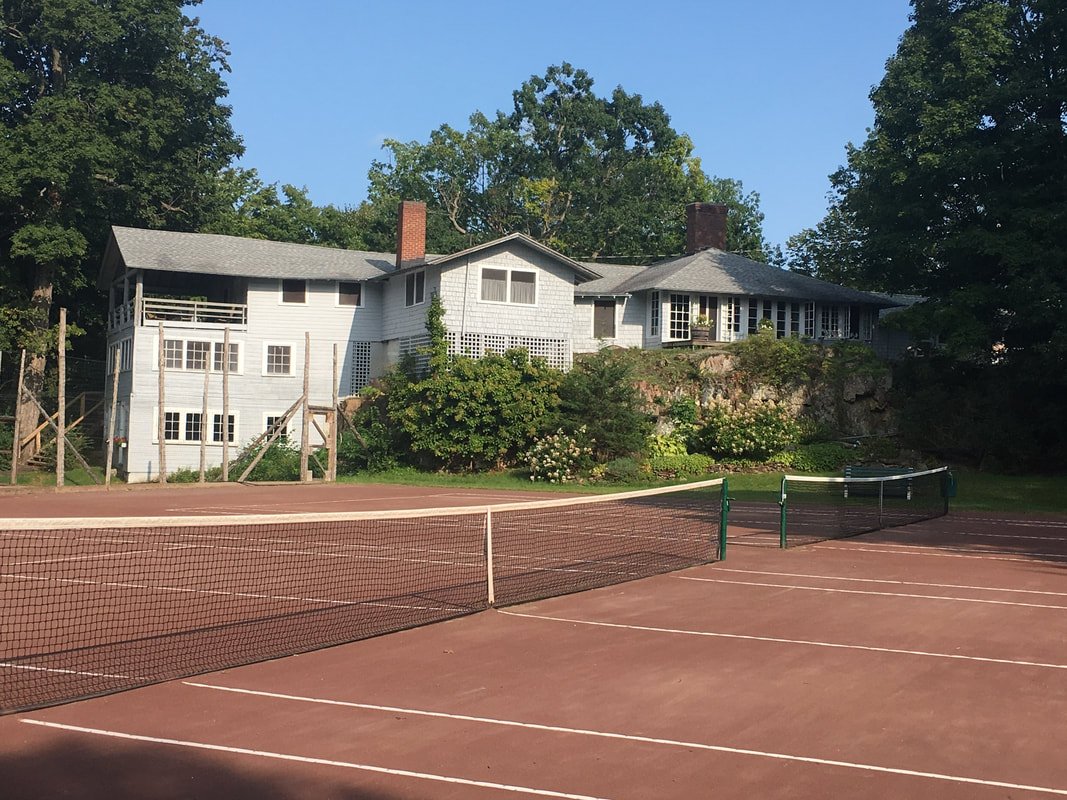 A tennis court with a house and trees in the background.